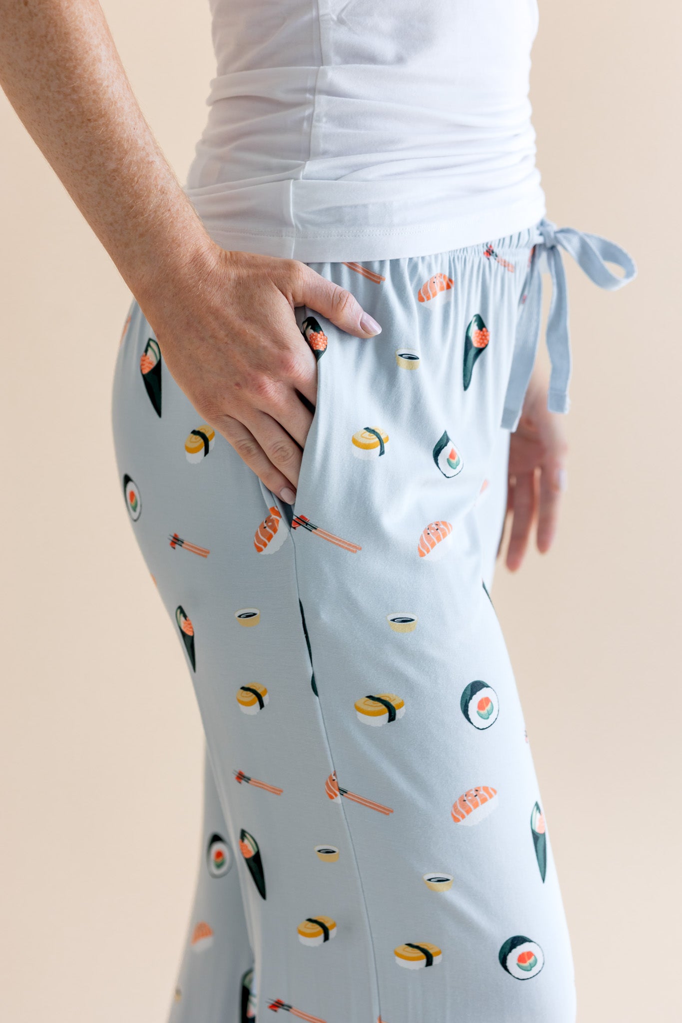 Model showing pockets of blue Women's Lounge Pants in Sushi print under white camisole on a beige background