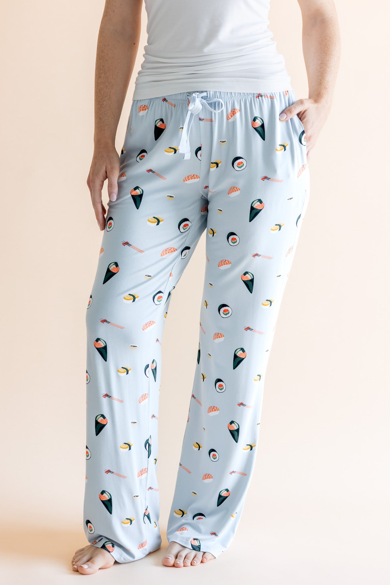 Model showing pockets of blue Women's Lounge Pants with drawstring in Sushi print under white camisole on a beige background