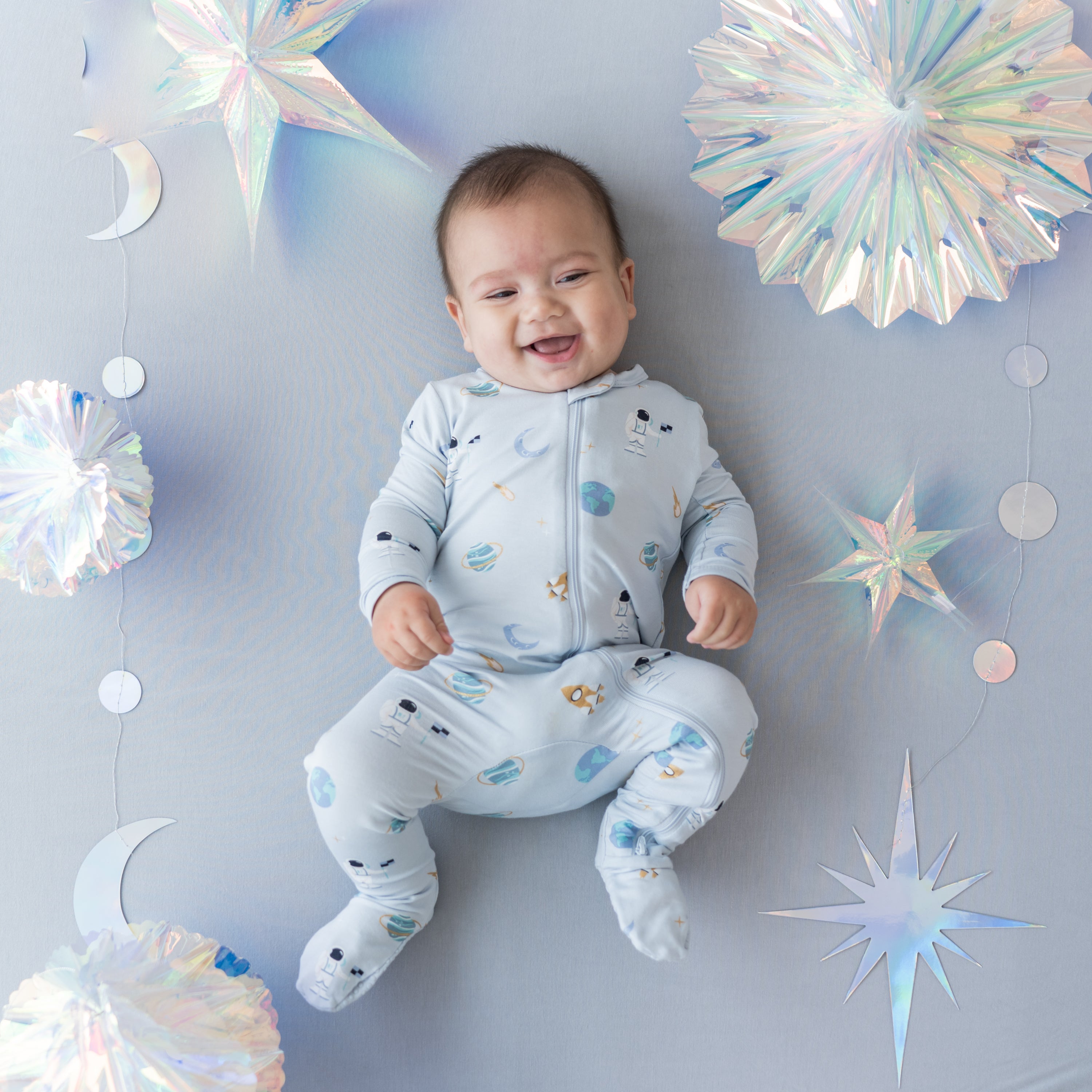 baby laying down and smiling wearing ice space zippered footie surrounded by metallic decorations