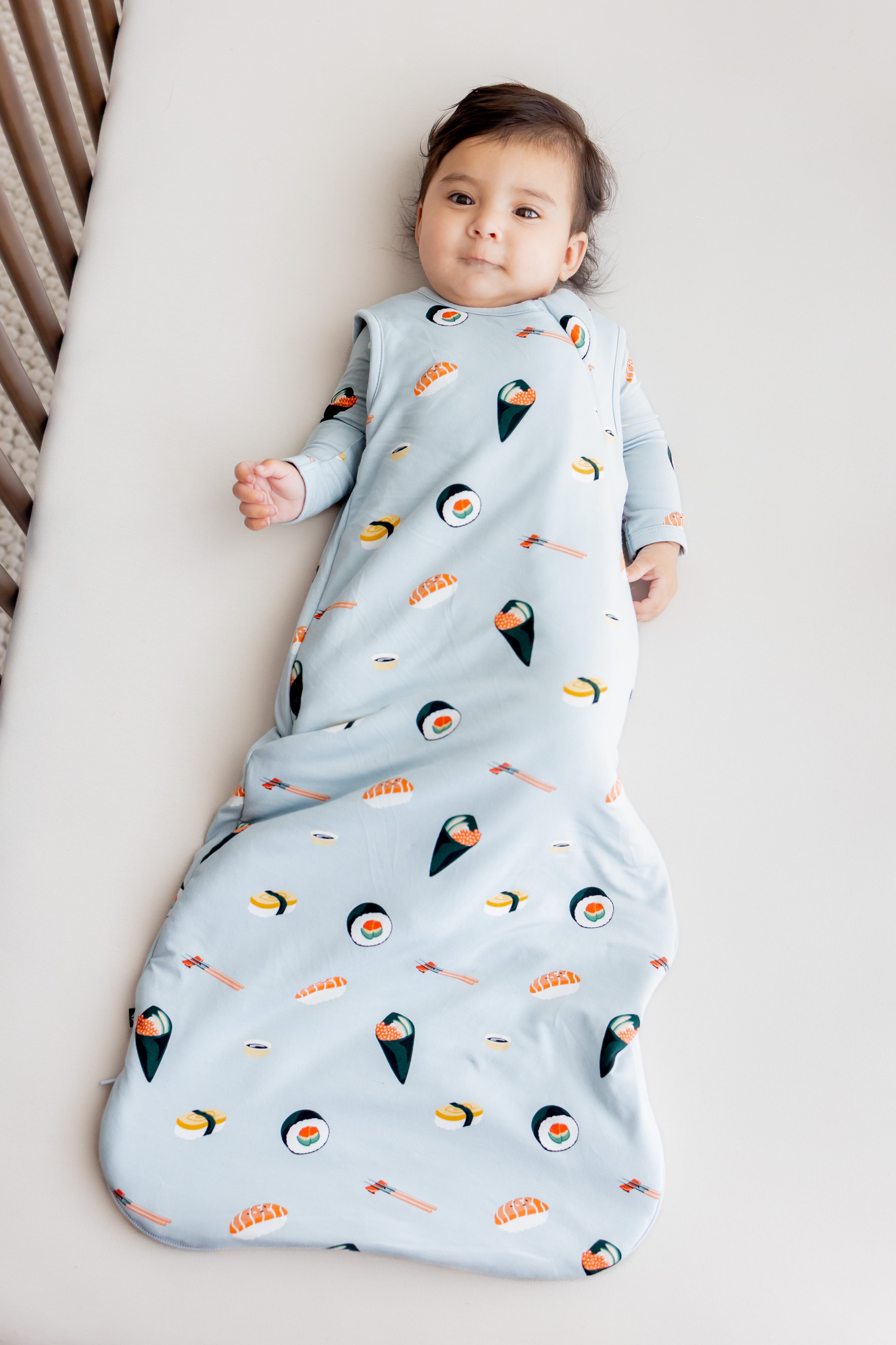 Baby laying in crib with white sheets in ice sushi sleep bag