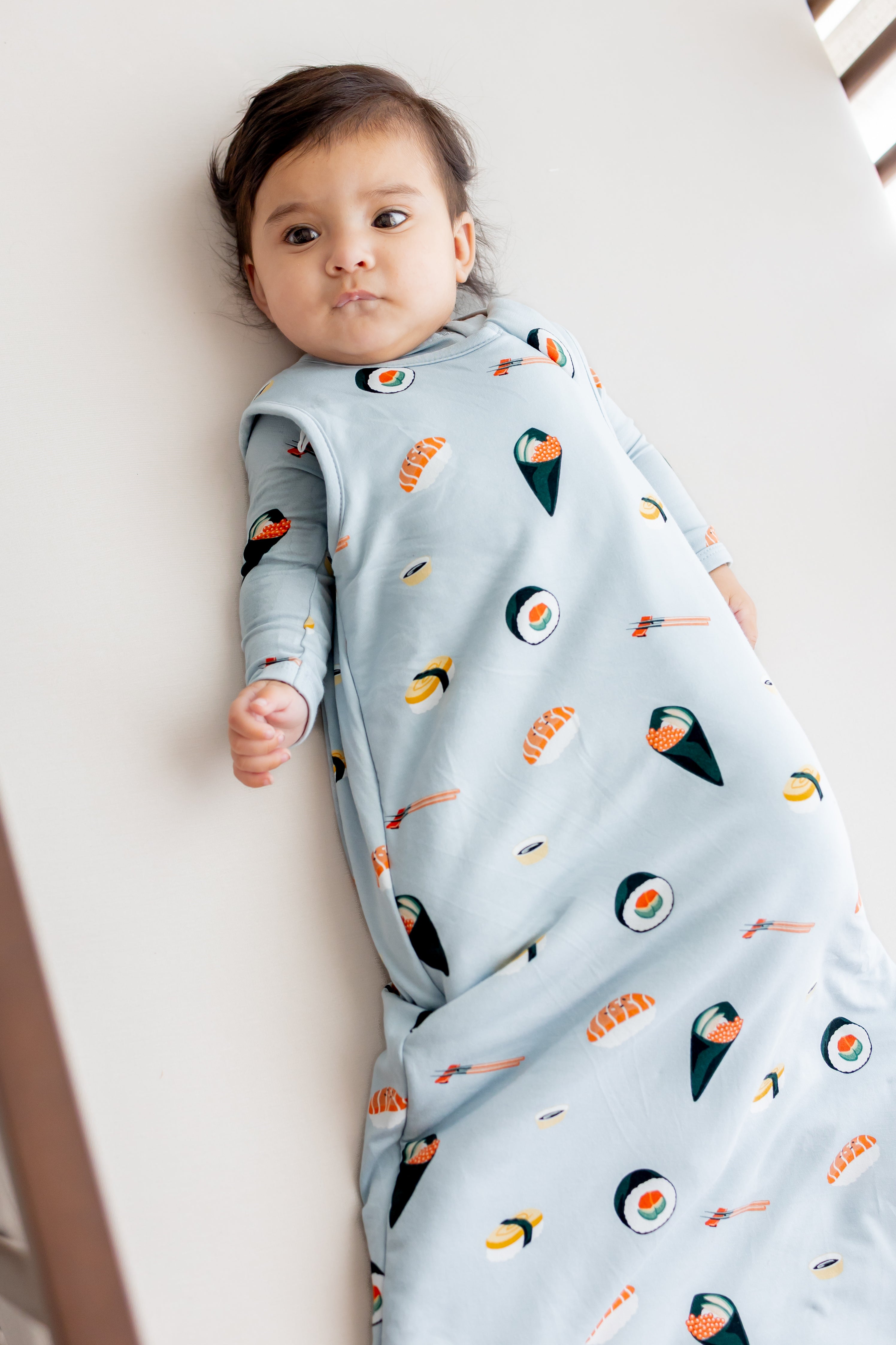 Baby laying in crib with white sheets in ice sushi sleep bag