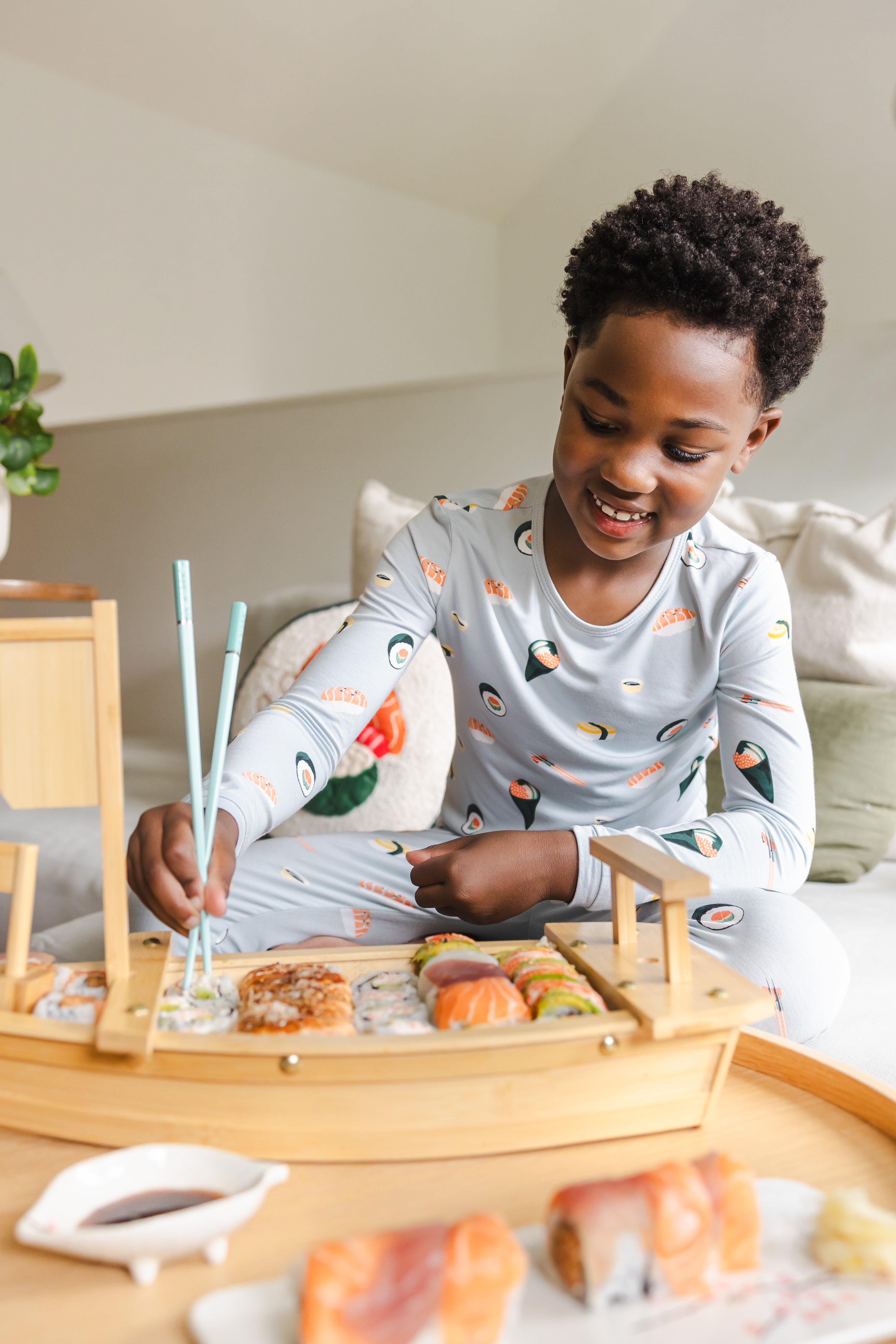 Child smiling down eating sushi with chop sicks in ice sushi pajama set