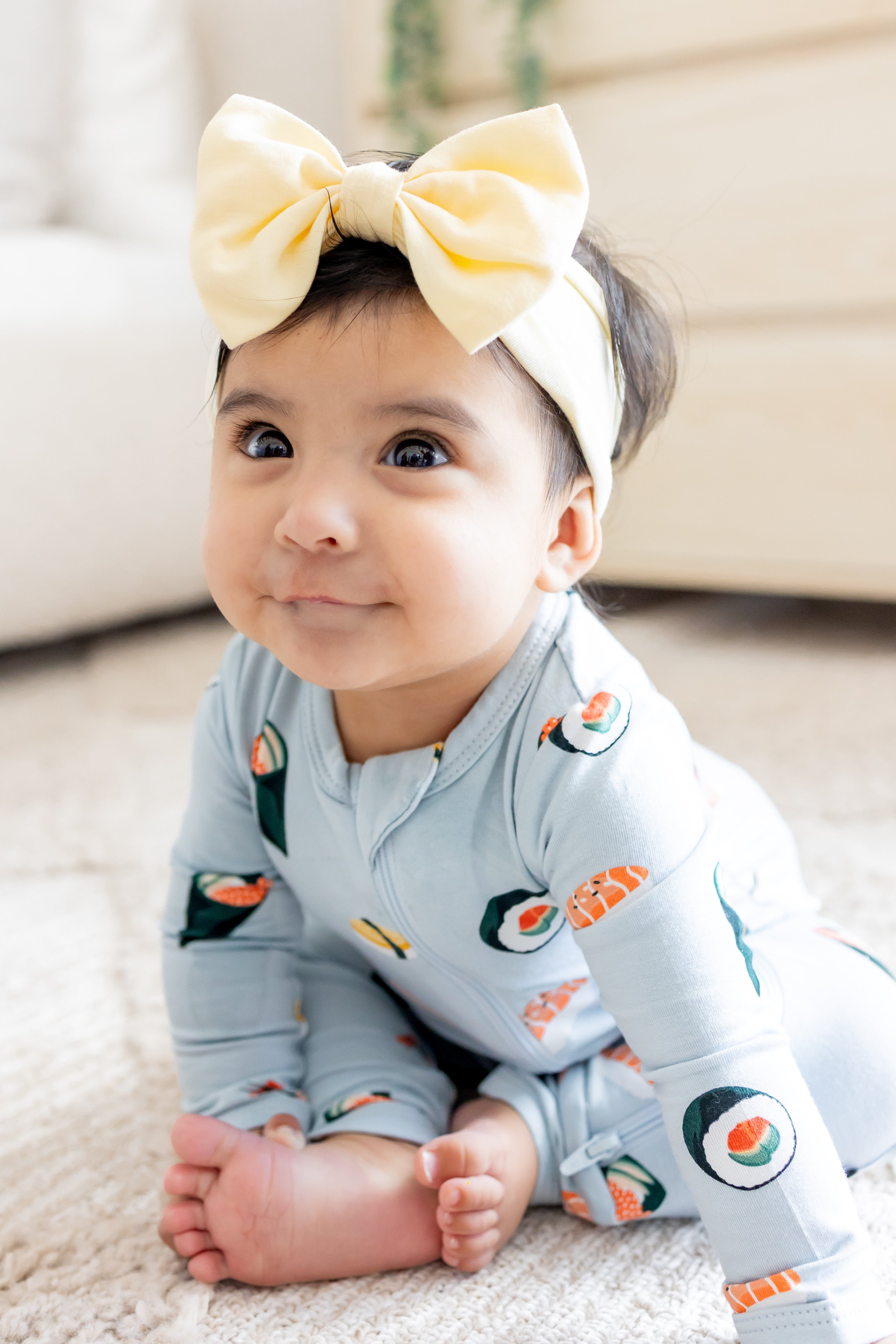 Baby sitting up in ice sushi zipper romper and a yellow bow