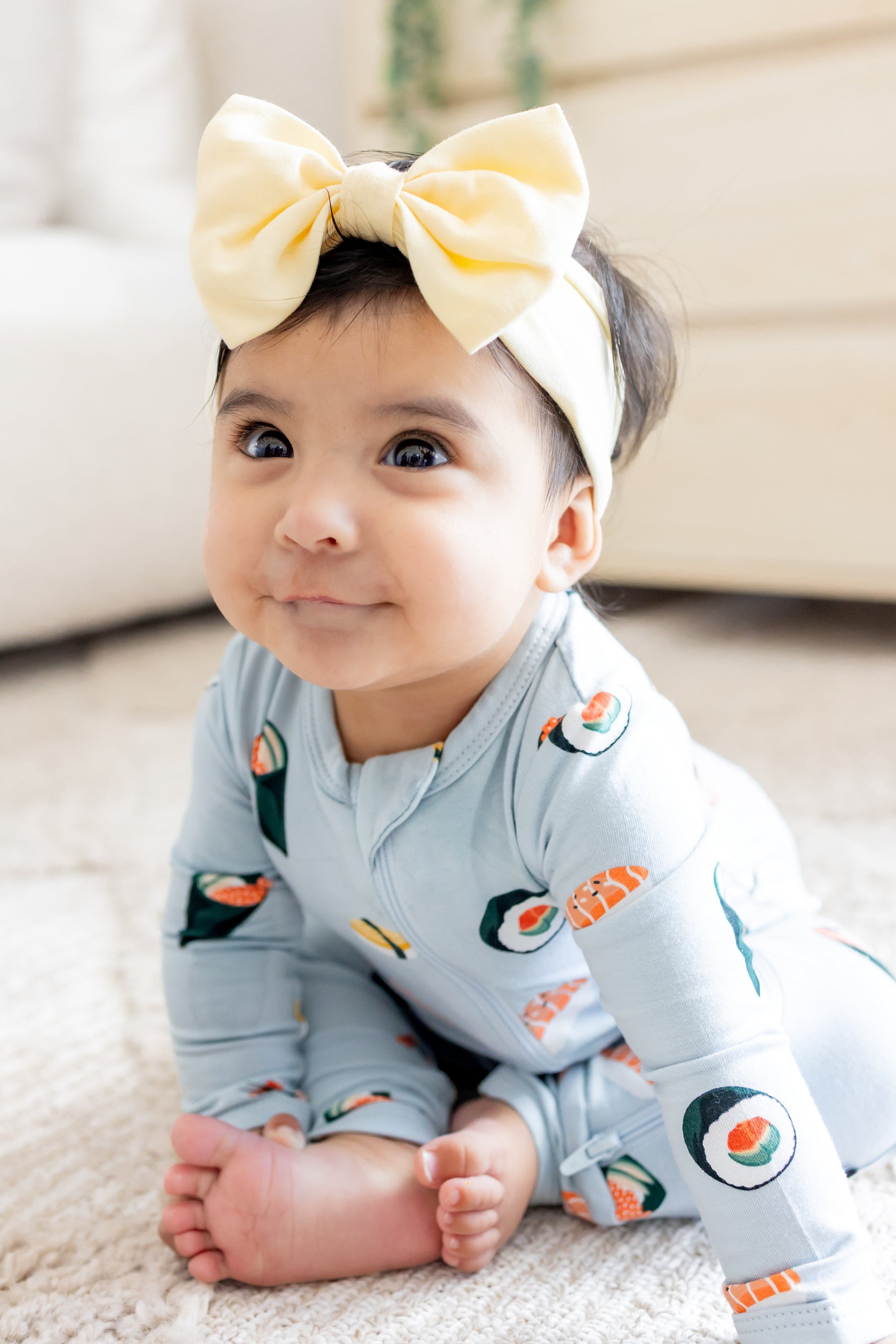 Baby sitting up in ice sushi zipper romper and a yellow bow