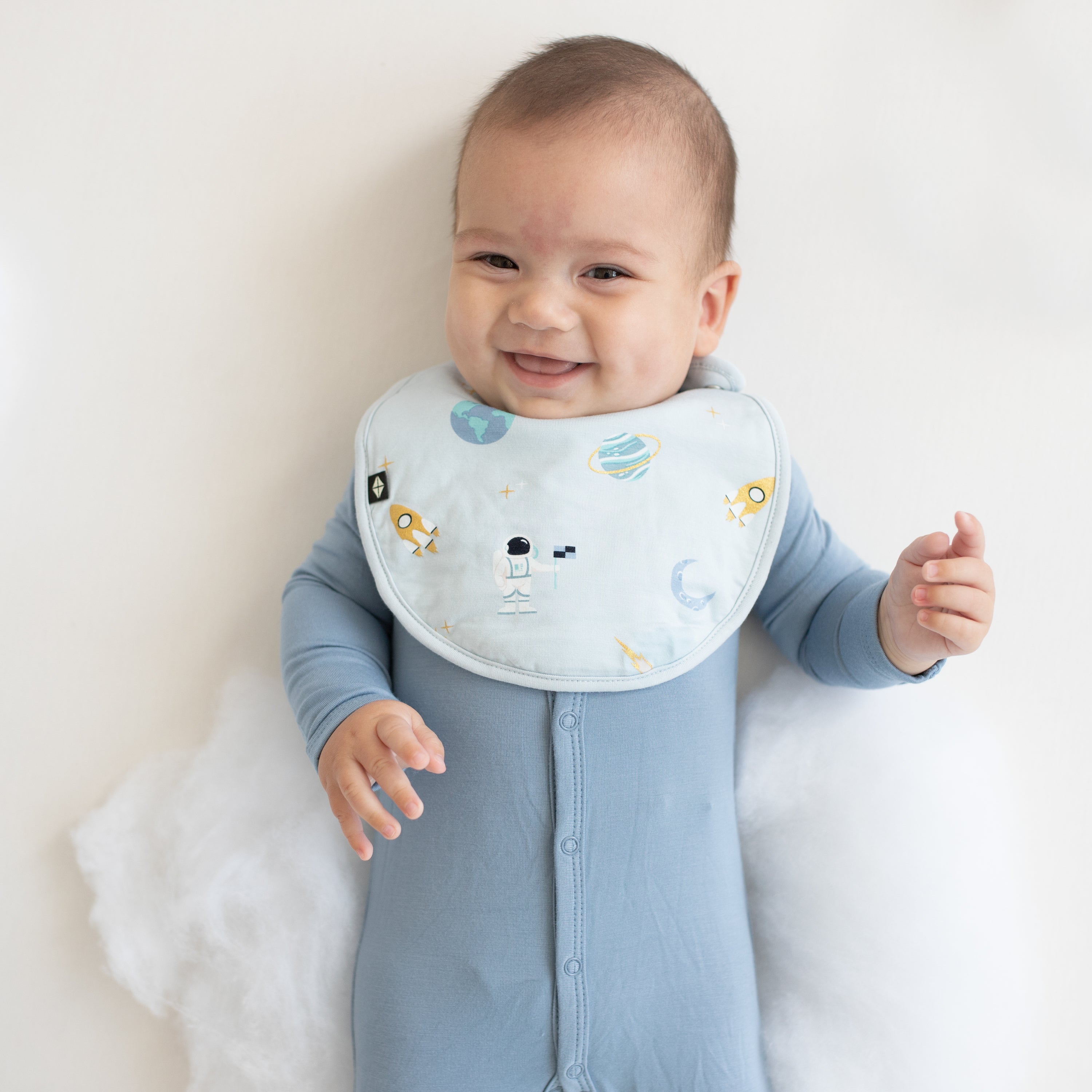 baby smiling wearing slate snap footie and ice space cushy bib