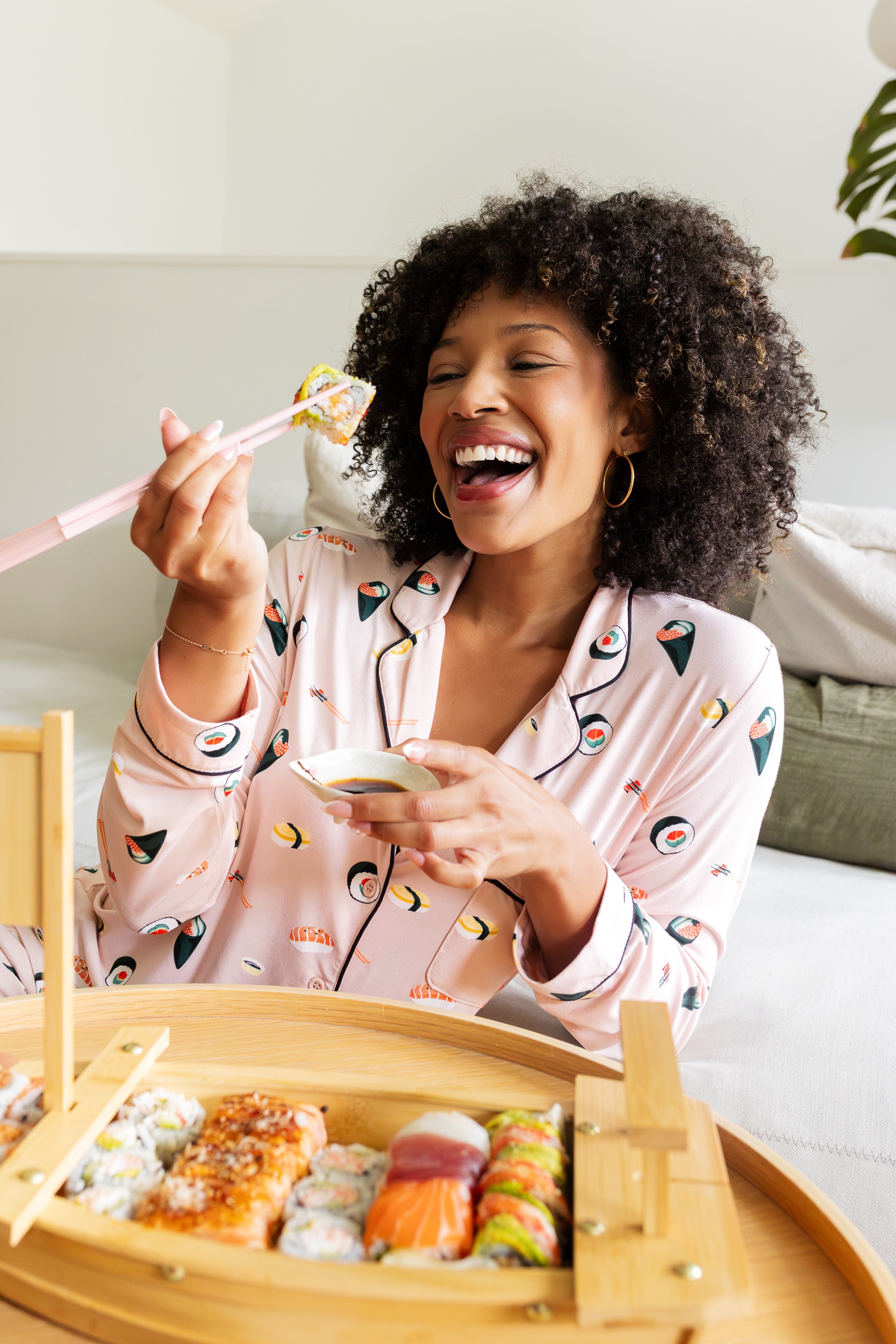 Woman in sushi print pajamas enjoying a meal of sushi with a bamboo tray.