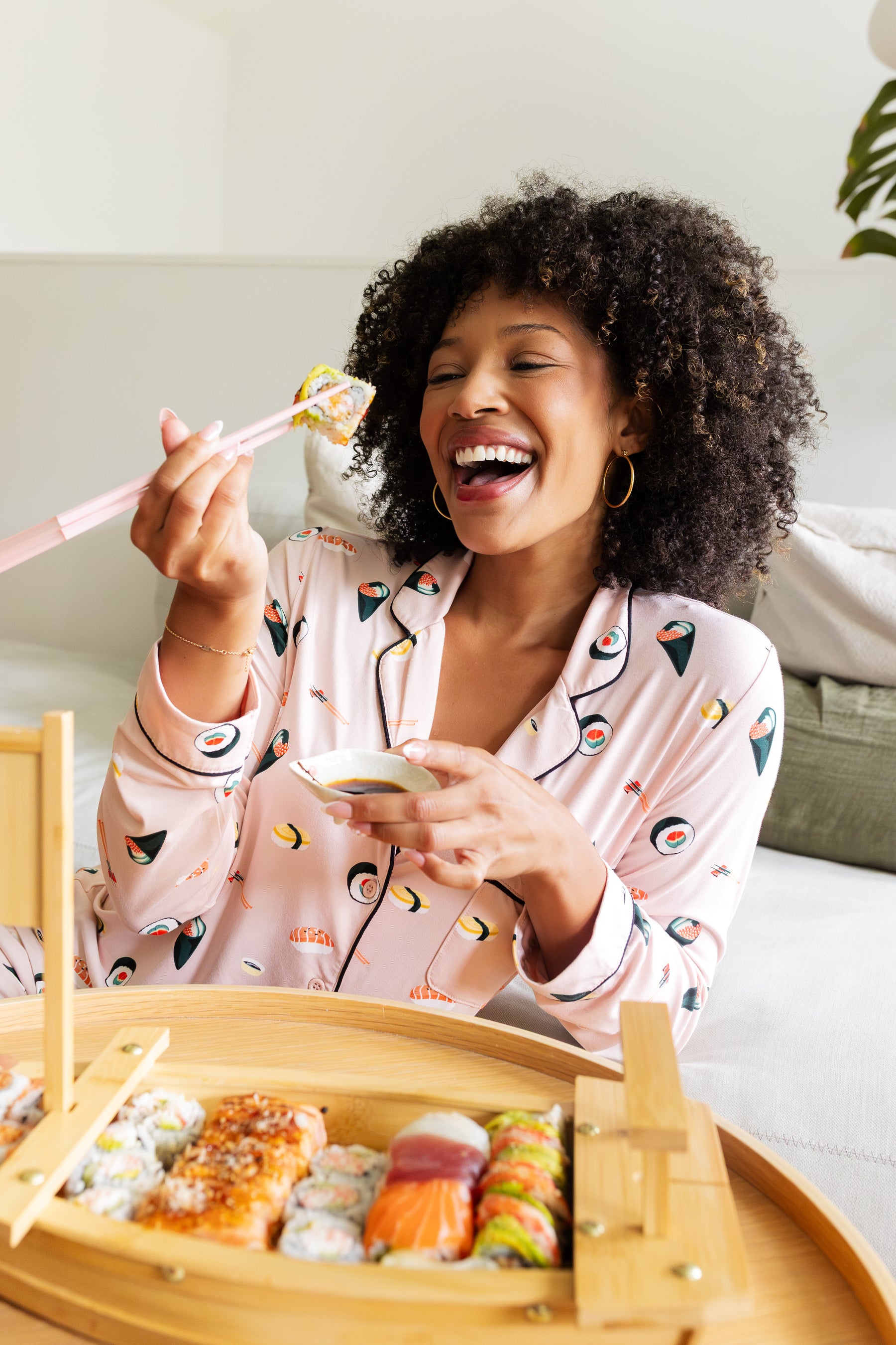 Woman in sushi print pajamas enjoying a meal of sushi with a bamboo tray.