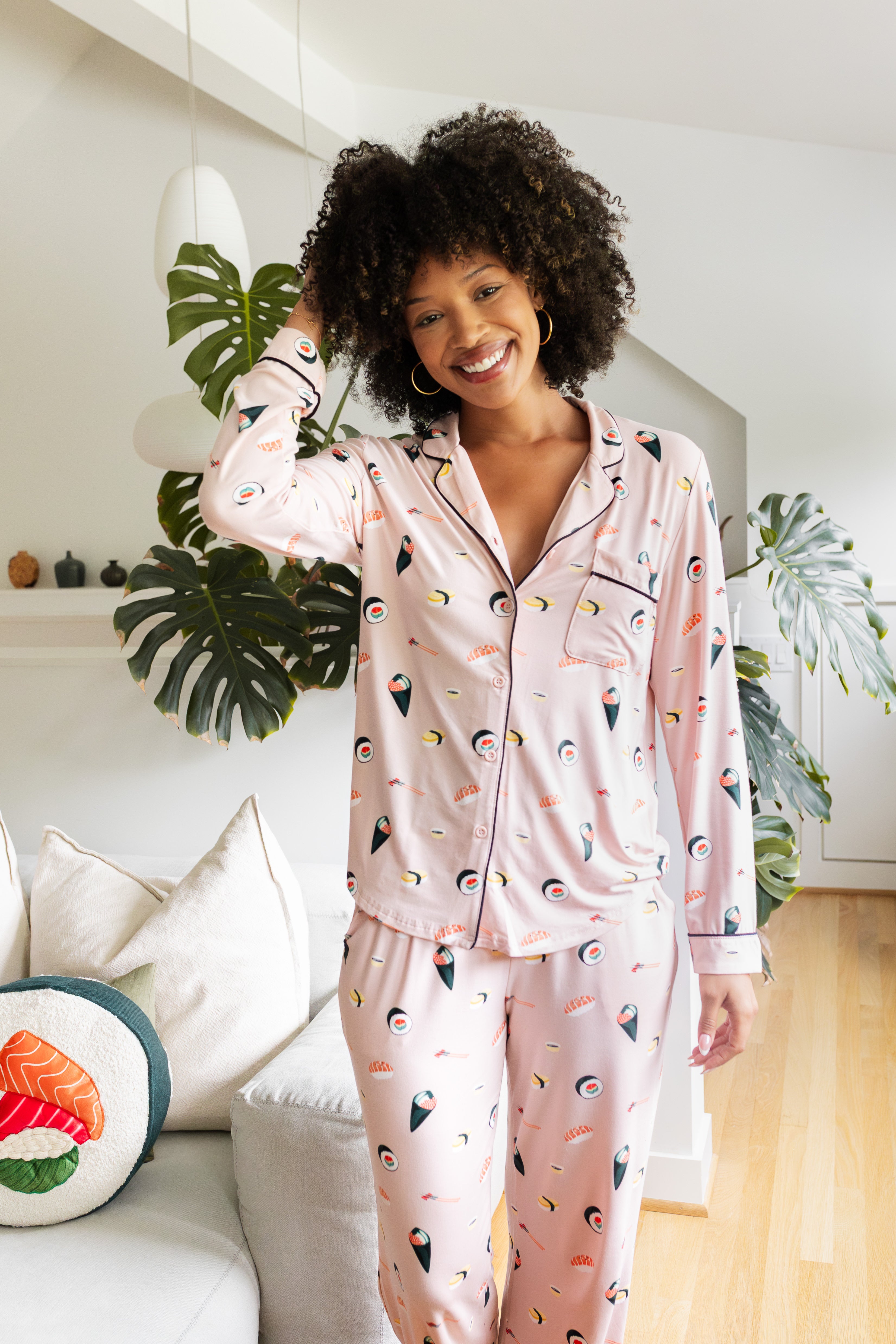Woman wearing a pink pajama set with sushi print in a cozy living room.