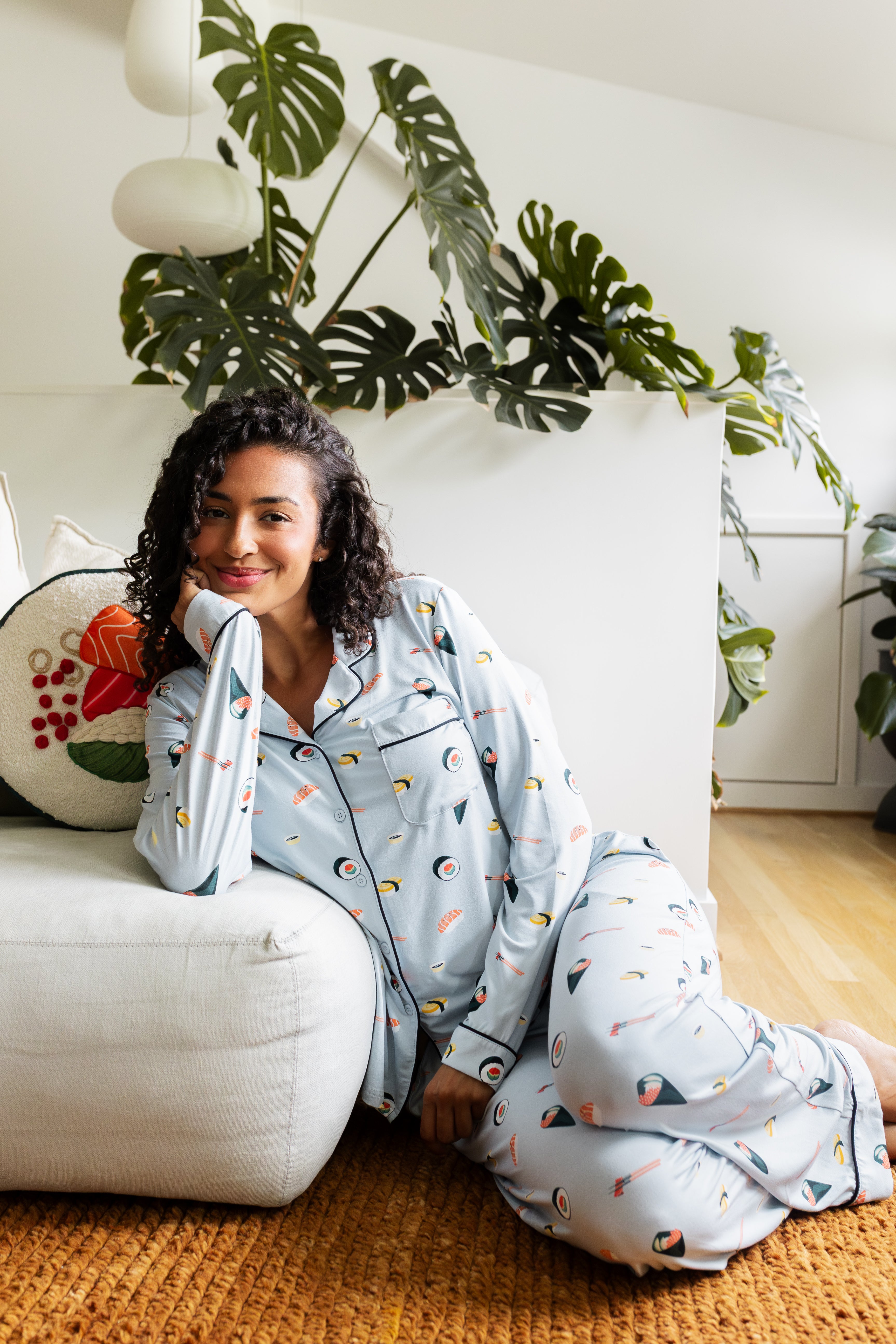 Woman sitting in a living room wearing a light blue pajama set with colorful sushi patterns