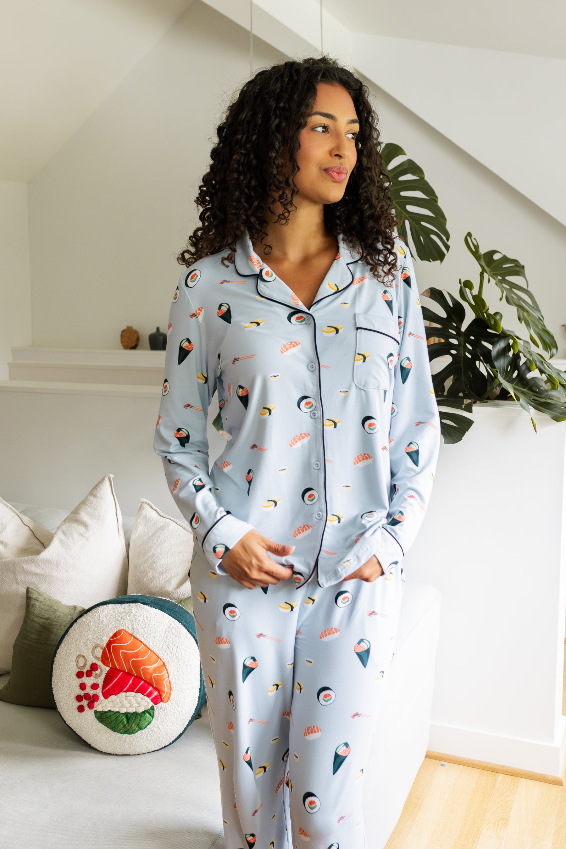 Woman wearing a light blue pajama set with colorful sushi patterns in a cozy living room.
