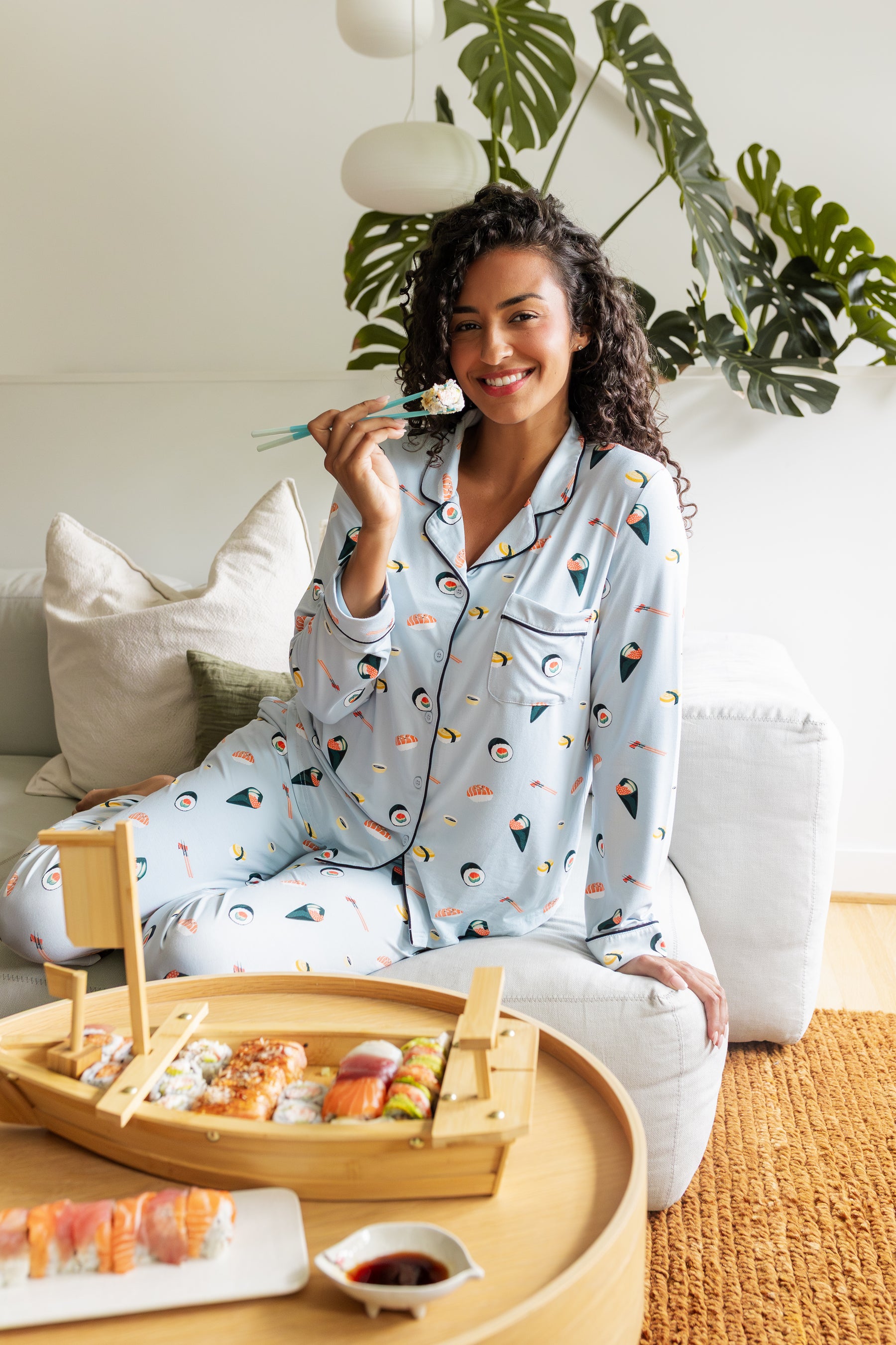 Woman in blue sushi print long sleeved pajamas enjoying a meal of sushi with a bamboo tray.