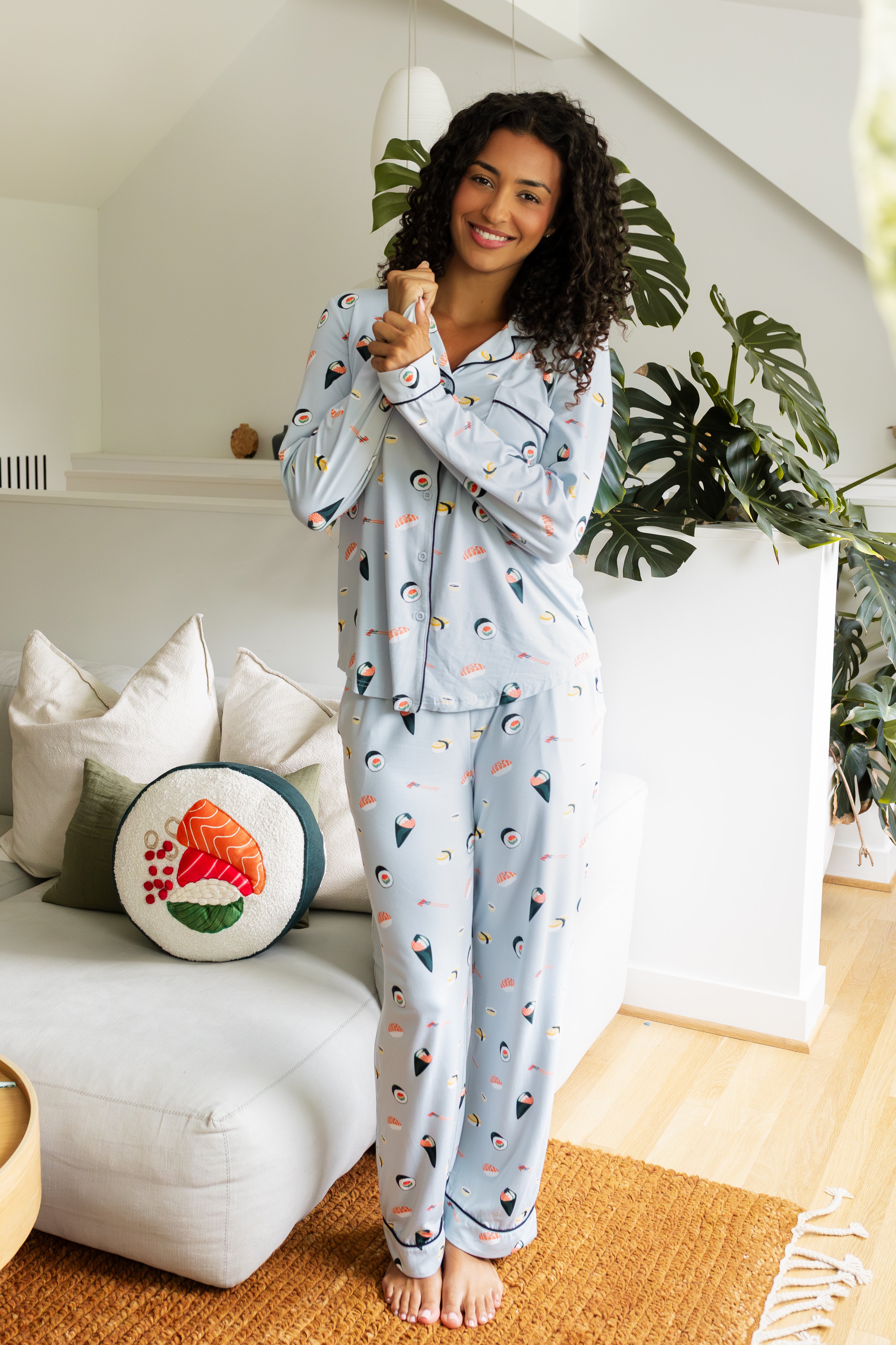 Woman wearing a light blue pajama set with colorful sushi patterns standing in a cozy living room.