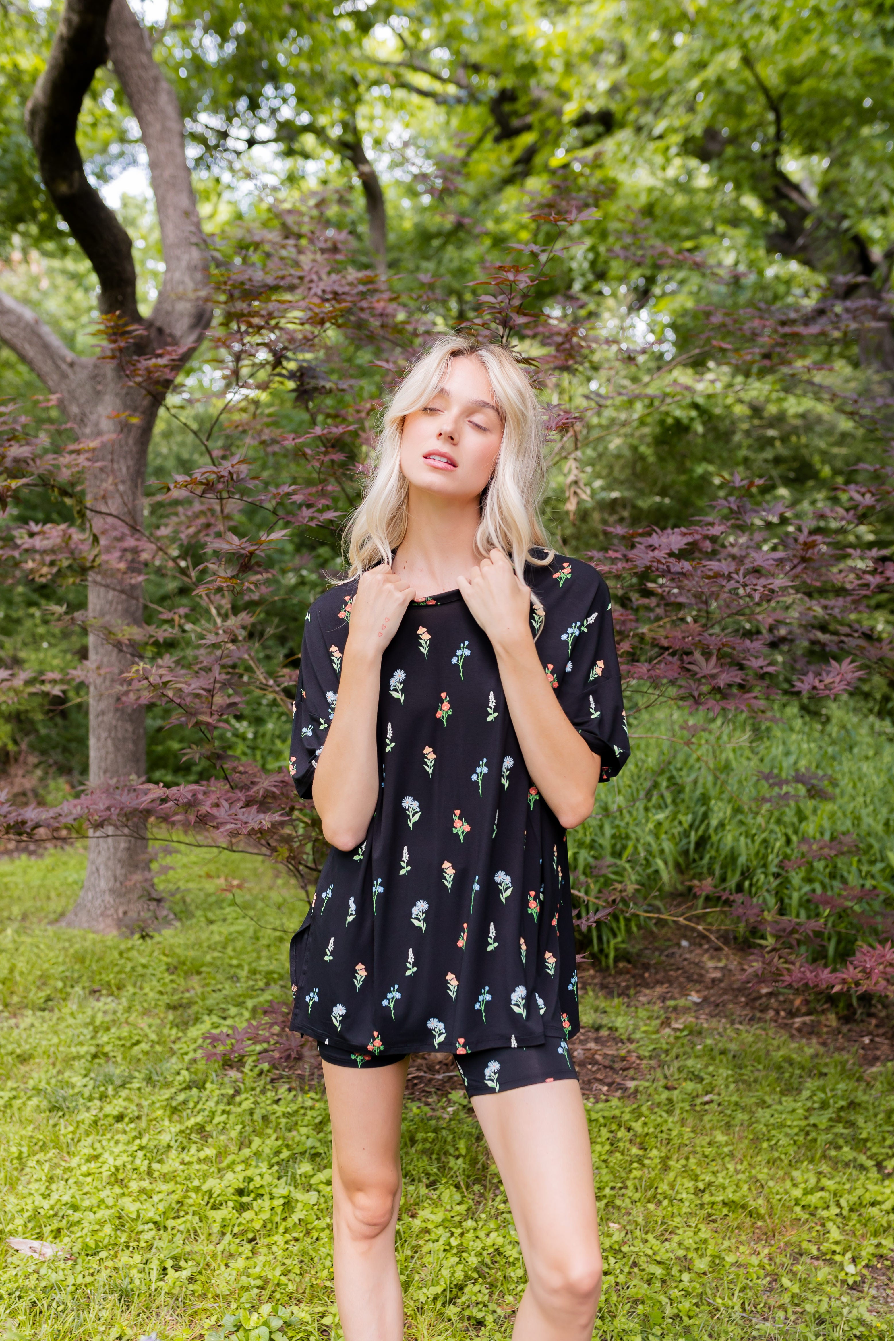 Model posing outdoors surrounded by trees wearing Women’s Biker Short Set in Midnight Wildflower print
