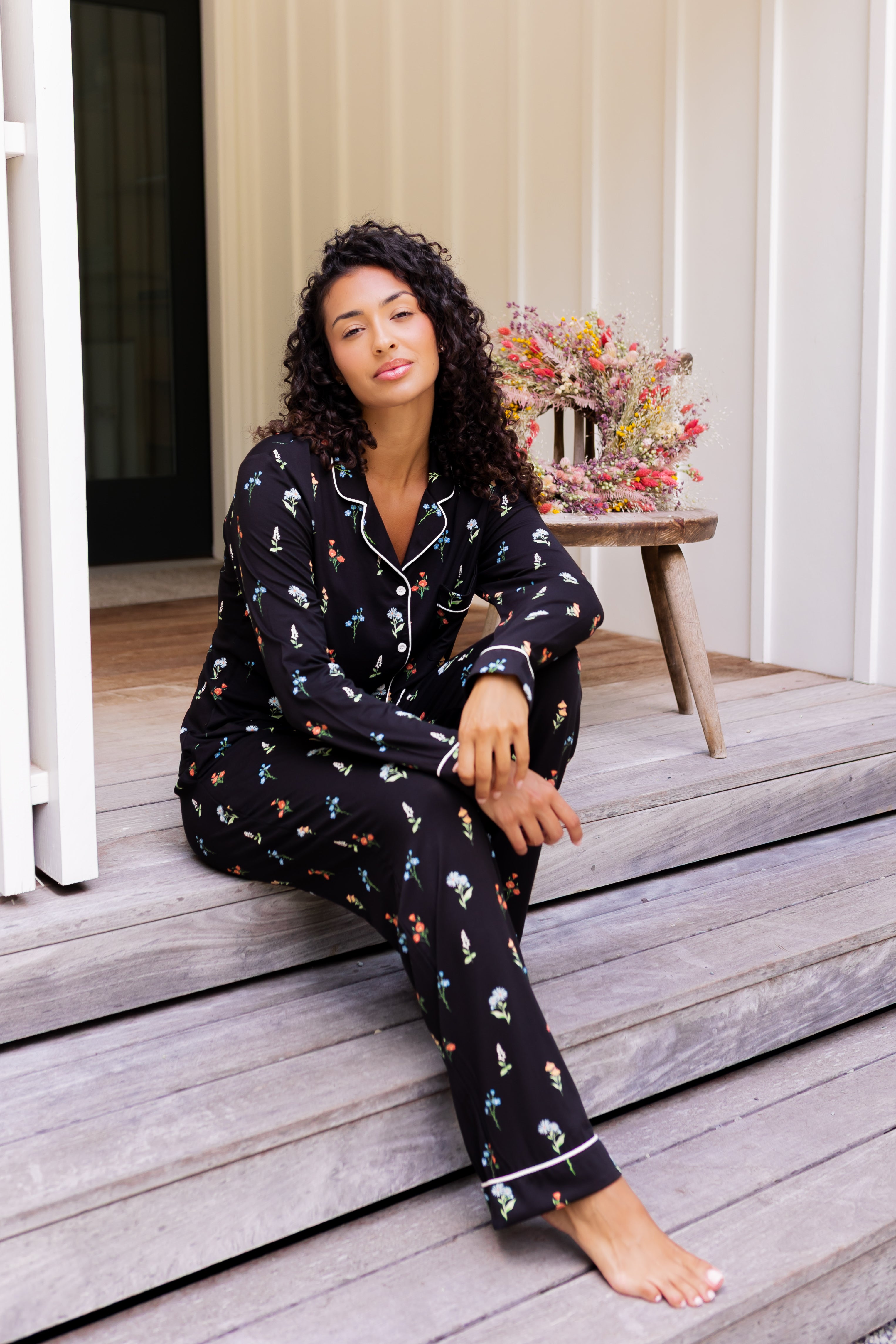 Model wearing Long-Sleeved Women's Pajama Set in Midnight Wildflower print sitting on outdoor steps