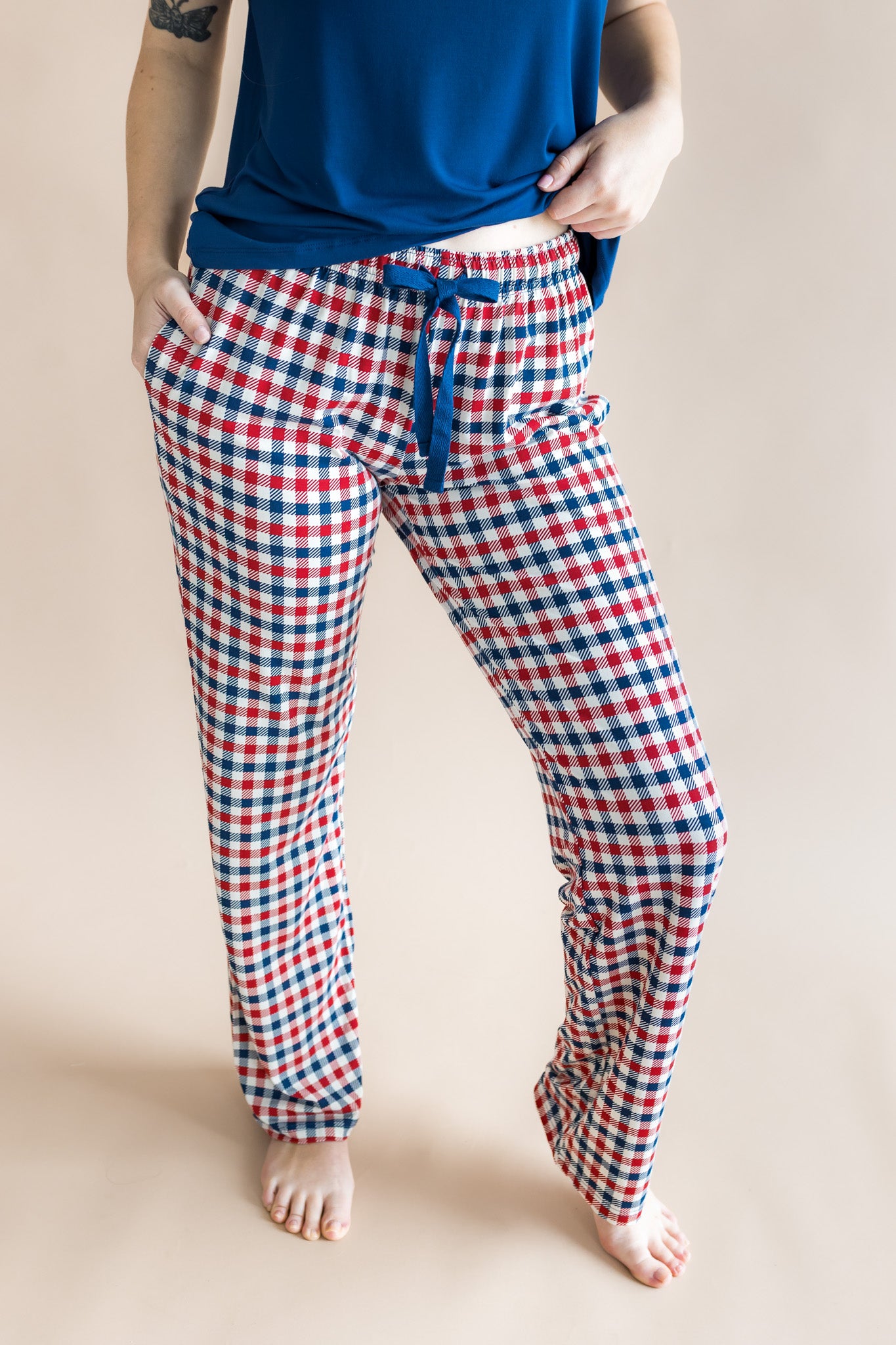 Model wearing women's lounge pants in red blue and white Patriotic Gingham check print under a navy shirt on a beige background