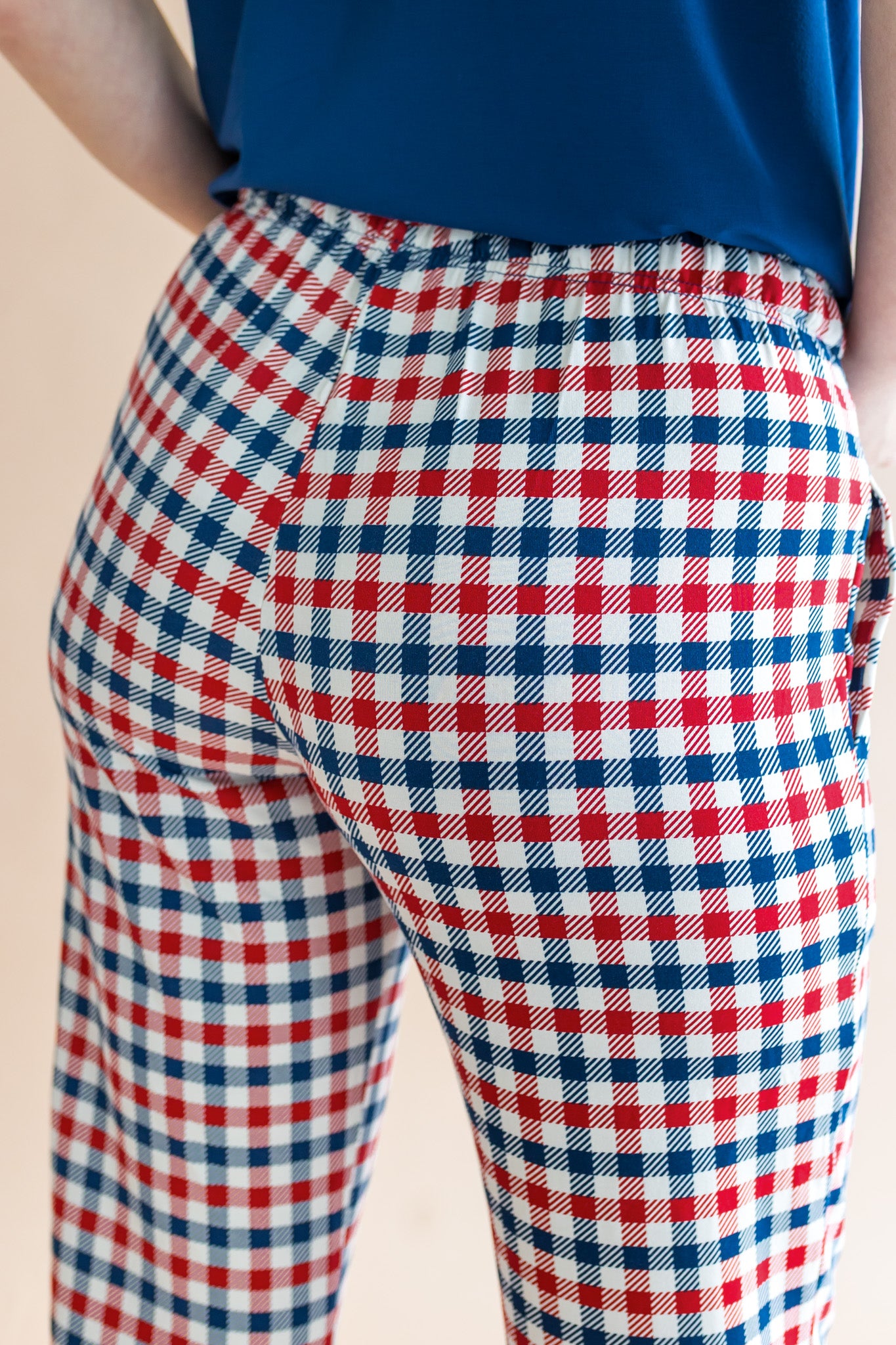 Back side of women's lounge pants in red blue and white Patriotic Gingham check print under a navy shirt on a beige background