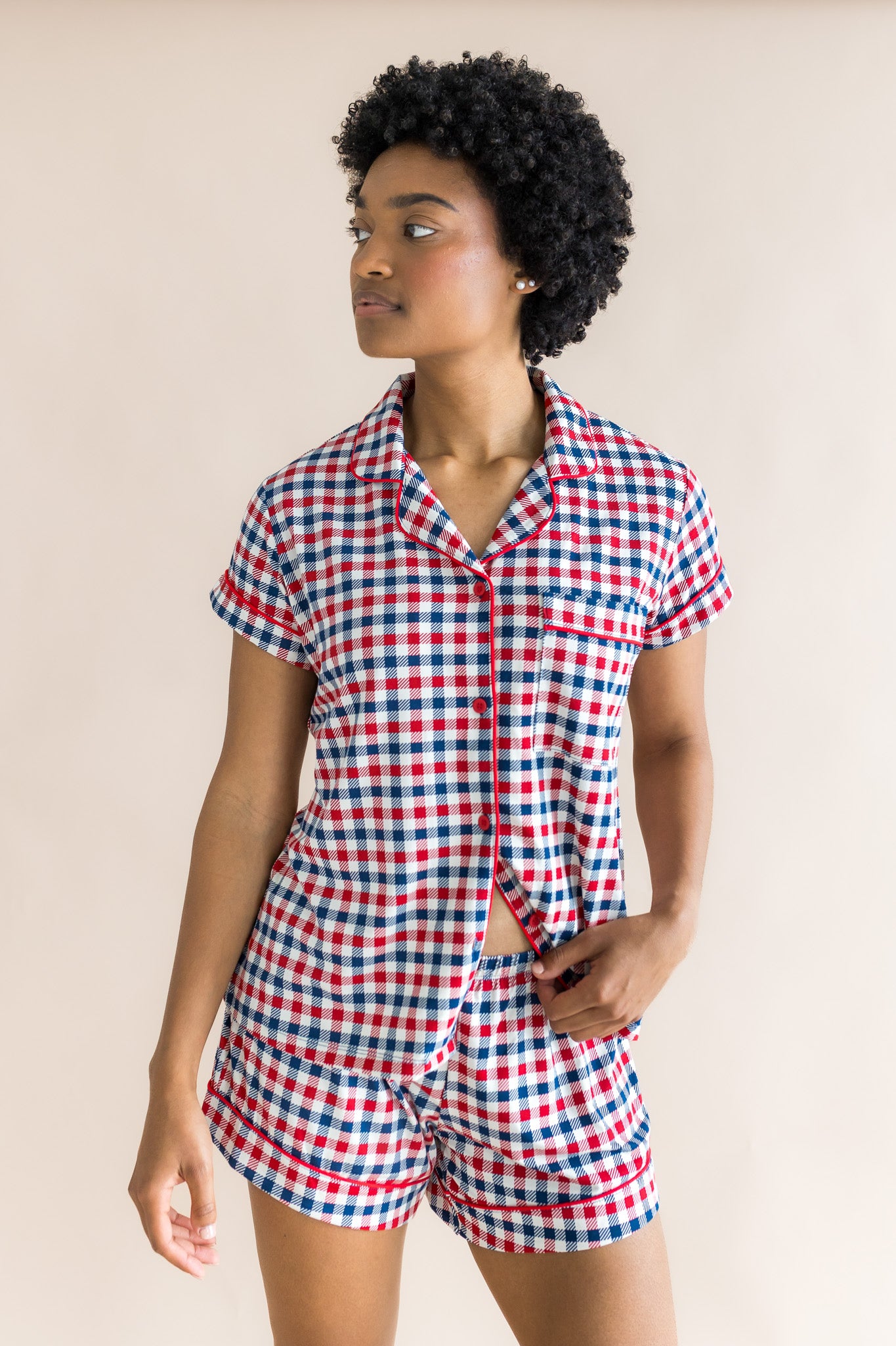 Model wearing women's short sleeve pajama set in red blue and white Patriotic Gingham check print on a beige background