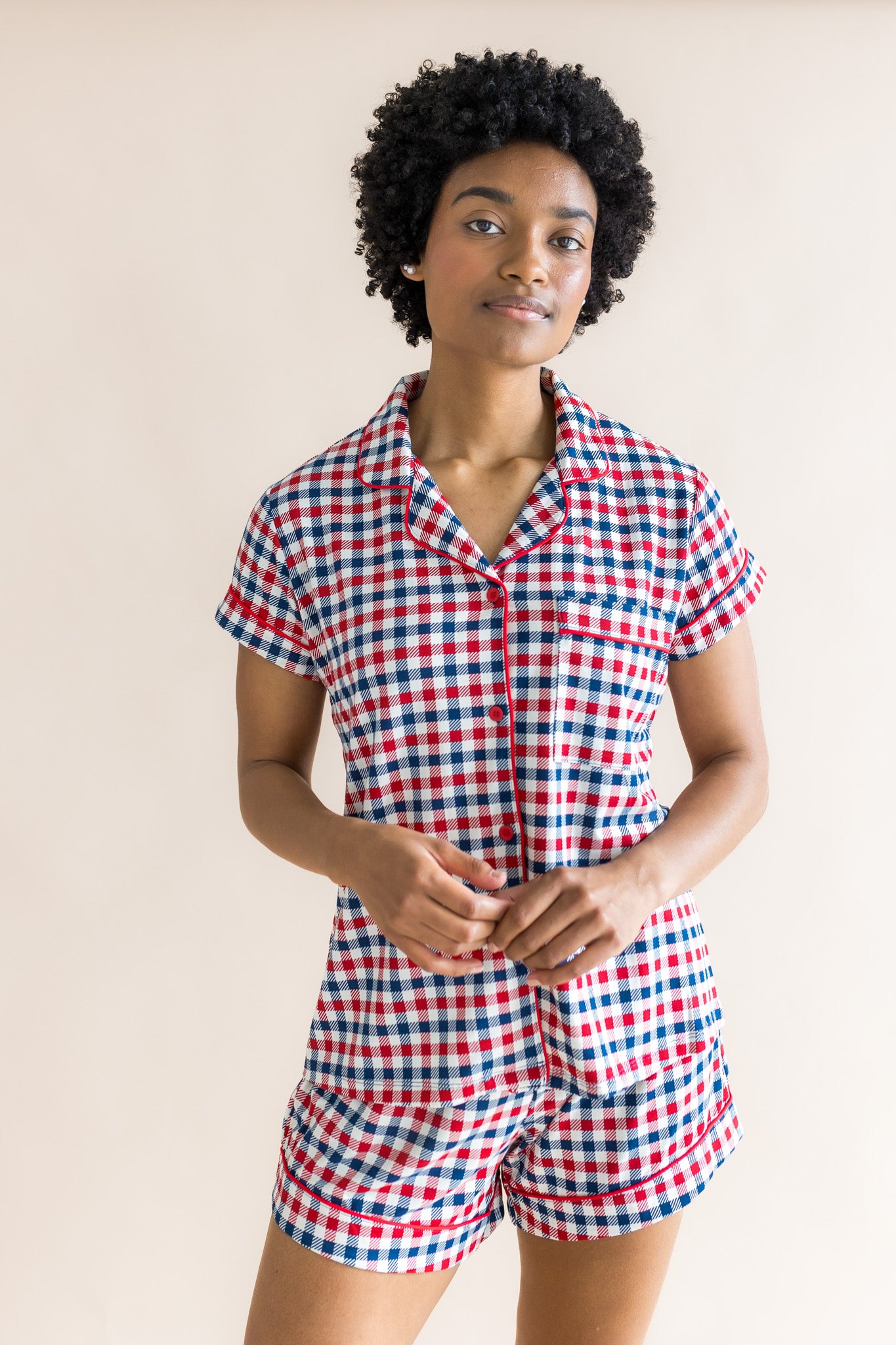 Model wearing women's short sleeve pajama set in red blue and white Patriotic Gingham check print on a beige background