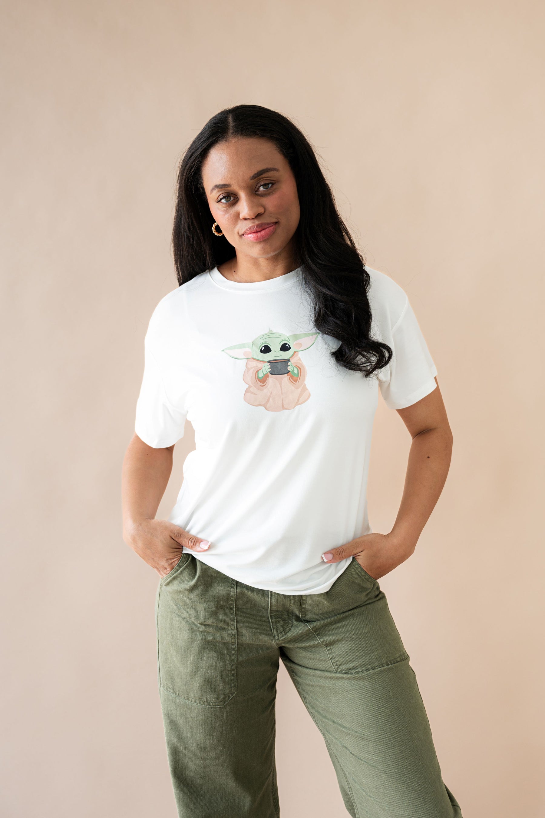 Female posing wearing the Women's Graphic Tee in The Child™ paired with dark green pants
