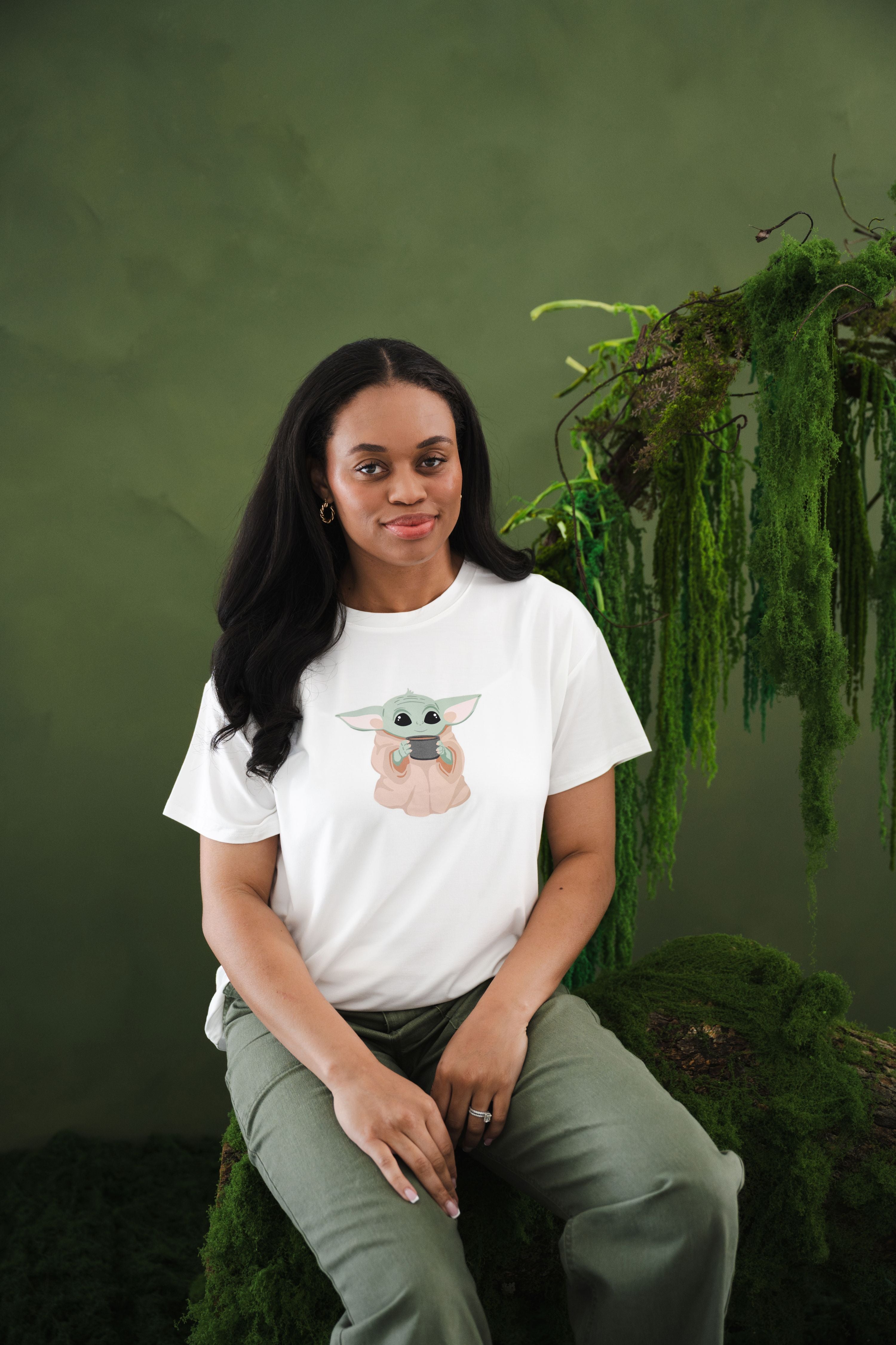 Female sitting on a tree stump with greenery on it wearing the Women's Graphic Tee in The Child™