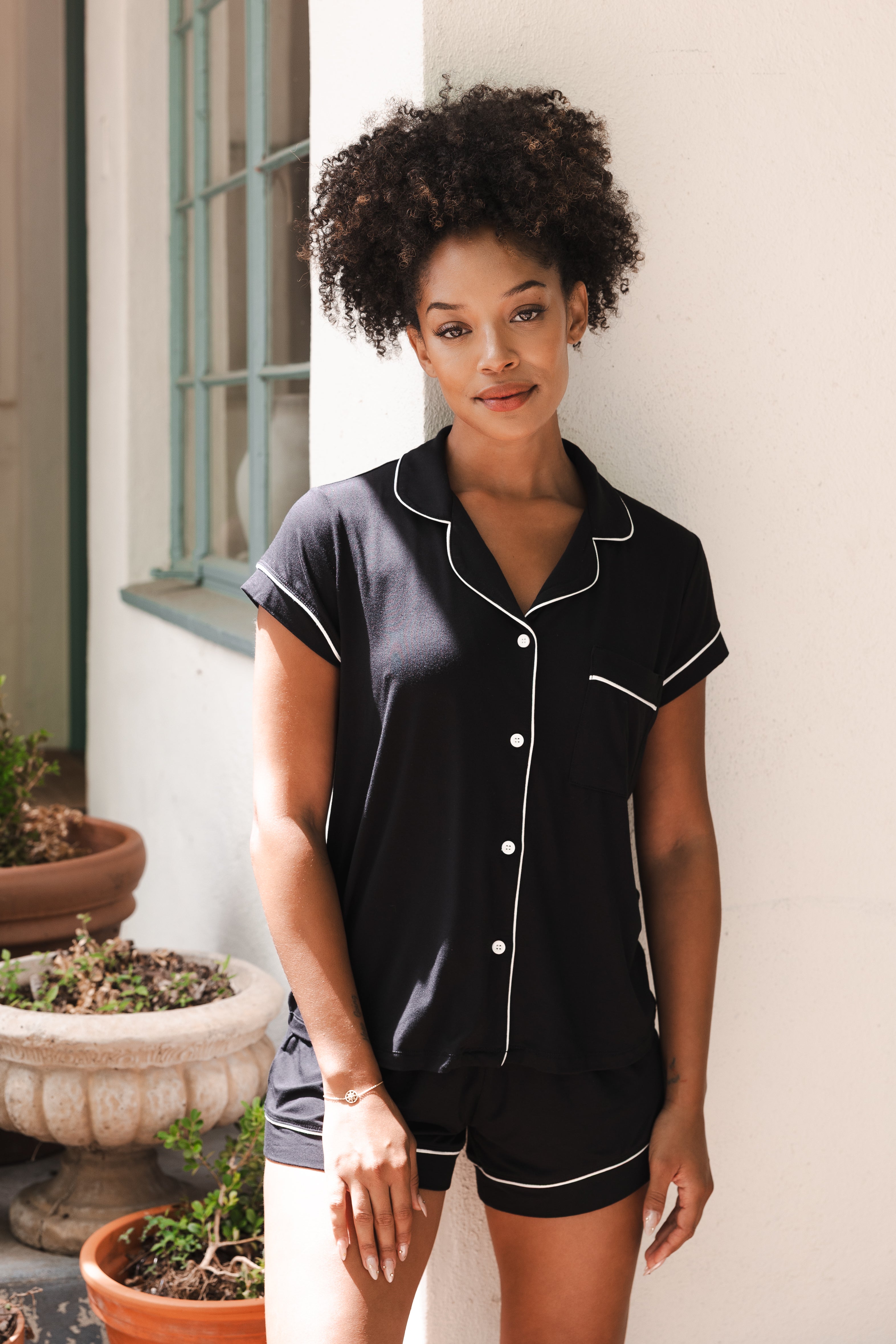 Female modeling the Women’s Short Sleeve Pajama Set in Midnight with Cloud Trim leaning against a white wall