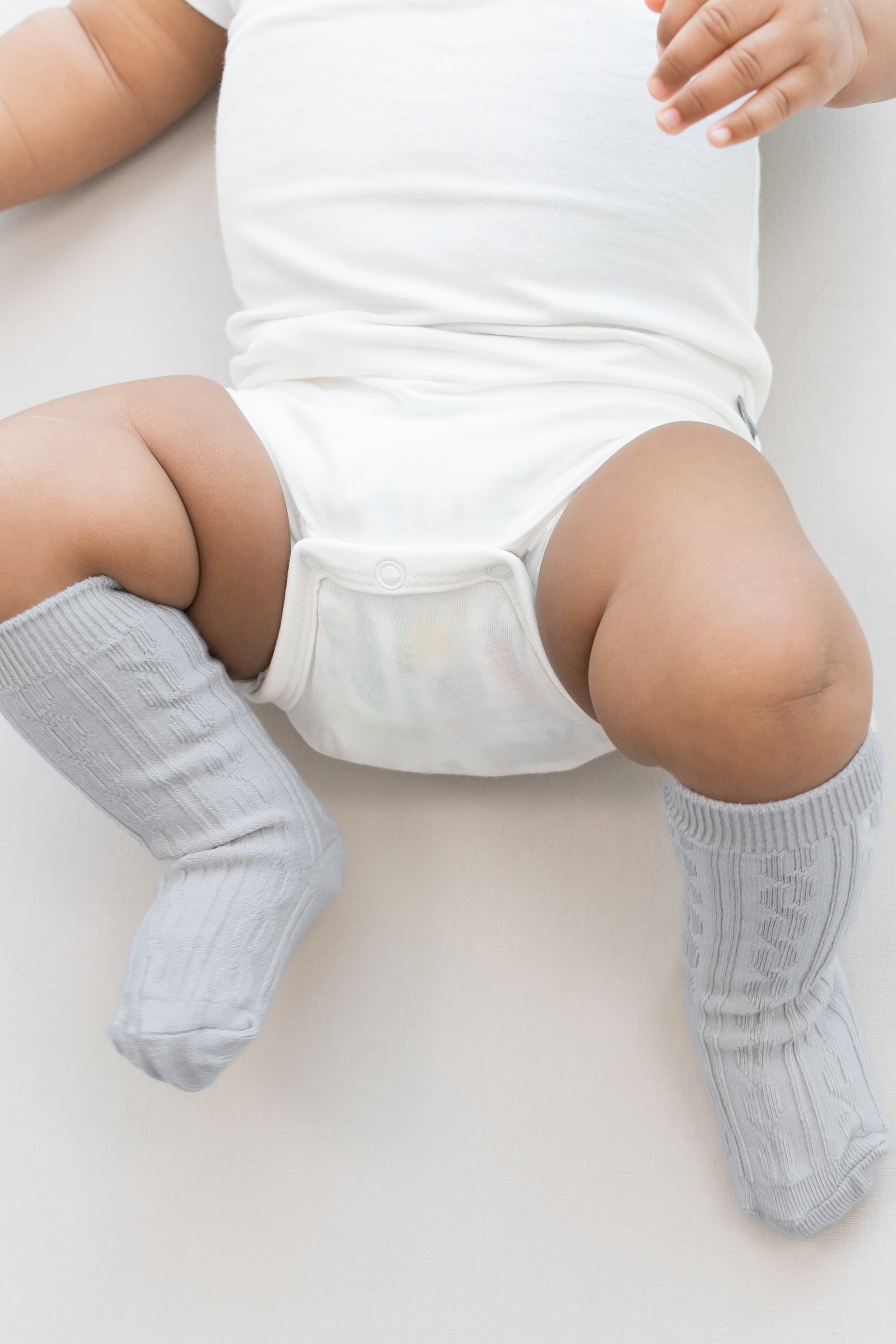 Close up of infant wearing the Knee High Socks in Storm paired with a Cloud bodysuit on a light neutral background