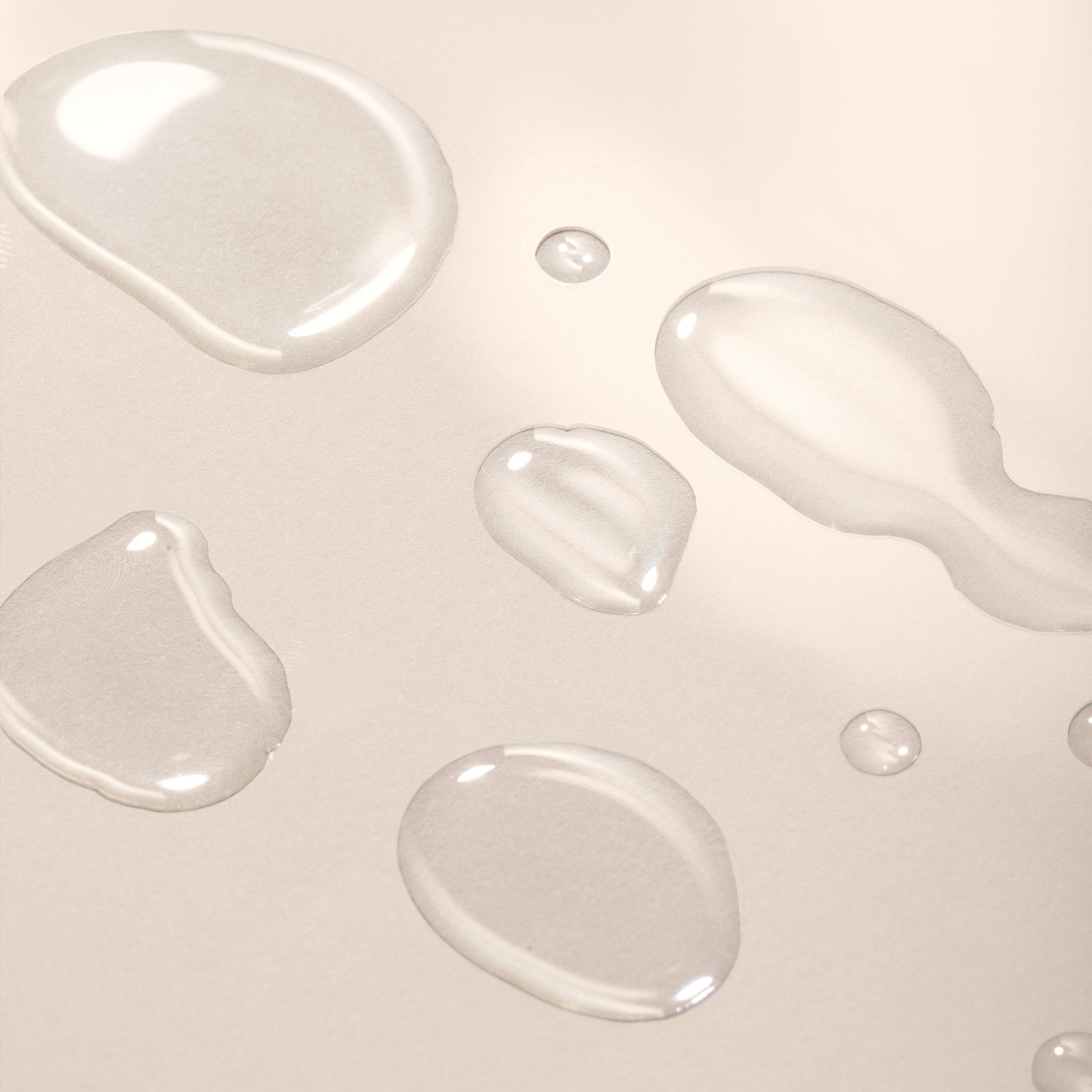 Close-up of clear liquid droplets on a light beige background