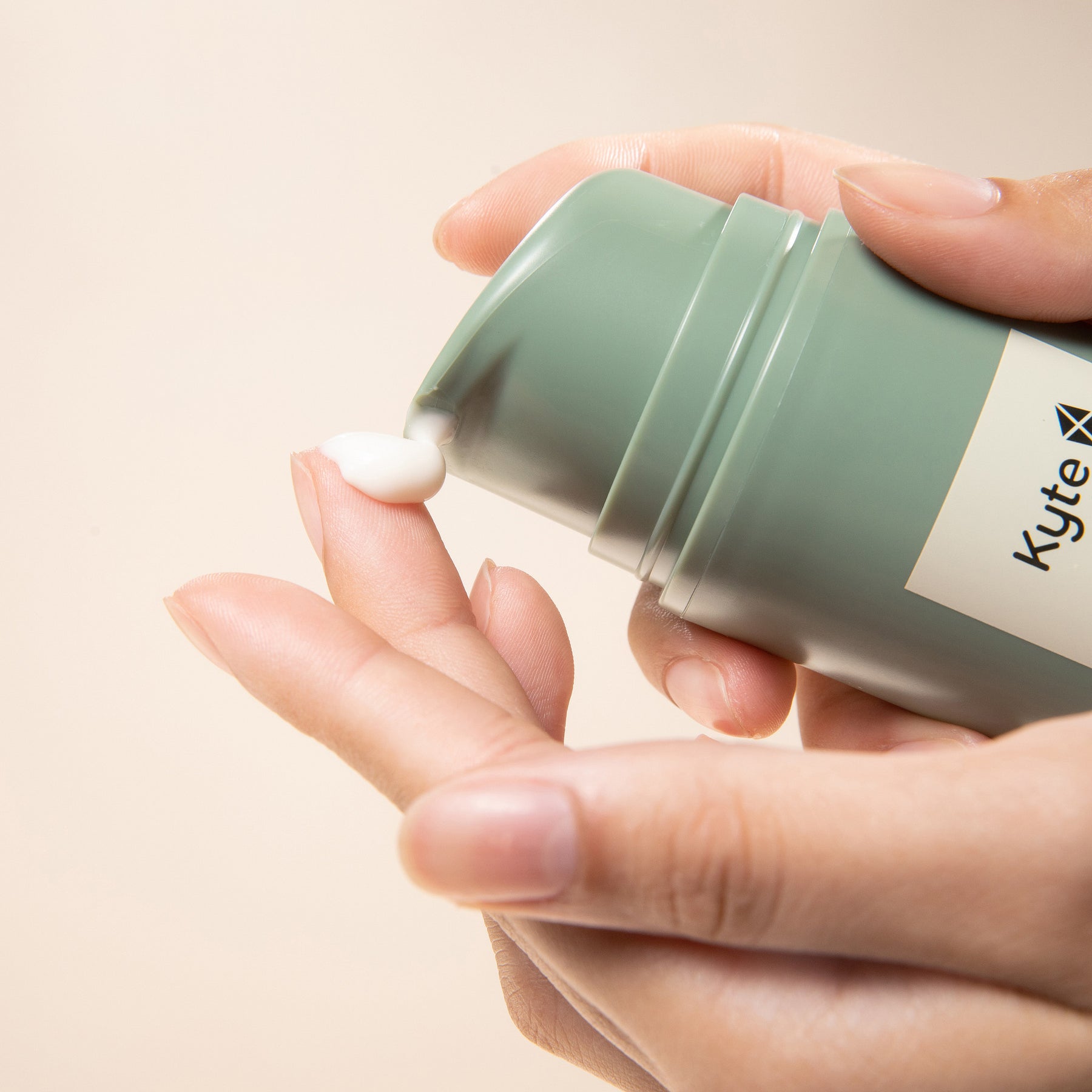 Hand holding a green container of Kyte skincare eczema cream with a beige background