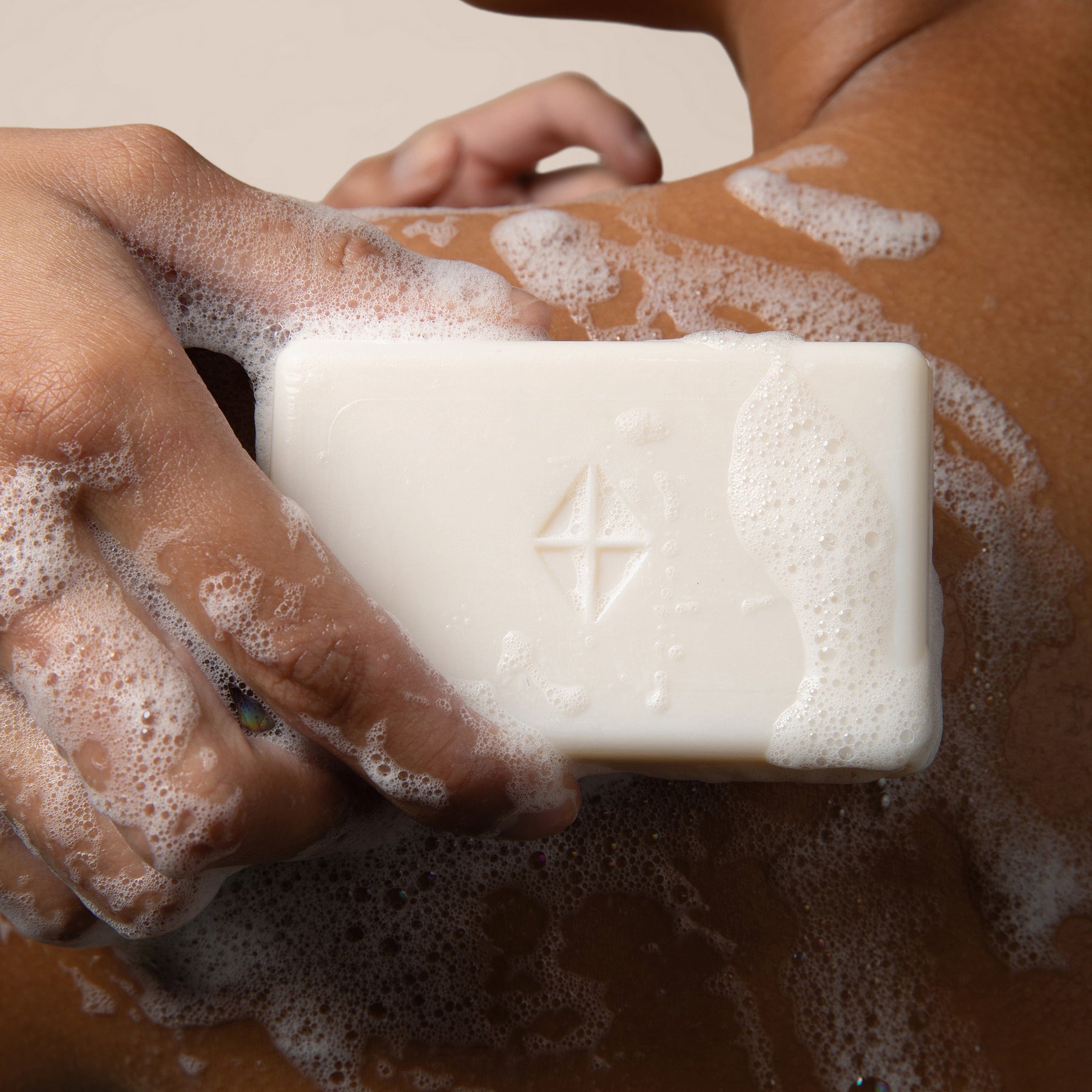 Bar of soap with a Kyte Skin logo held by soapy hands on a soapy surface