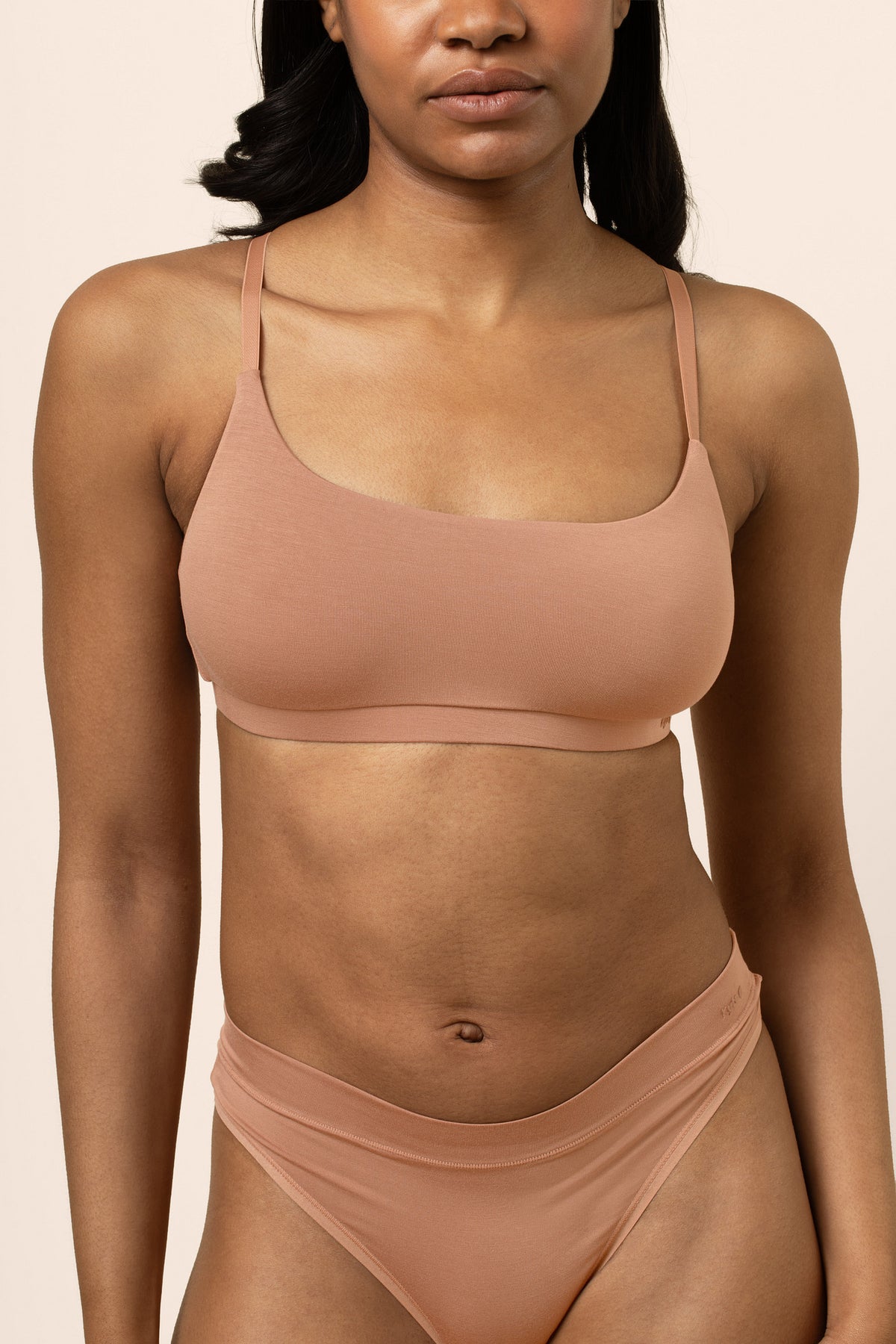 Woman wearing a buttery soft, tan scoop neck bralette  set against a beige background