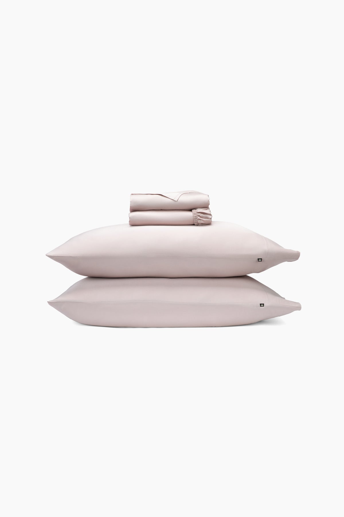 Set of light pink bedding including two pillows and a folded sheets on a white background