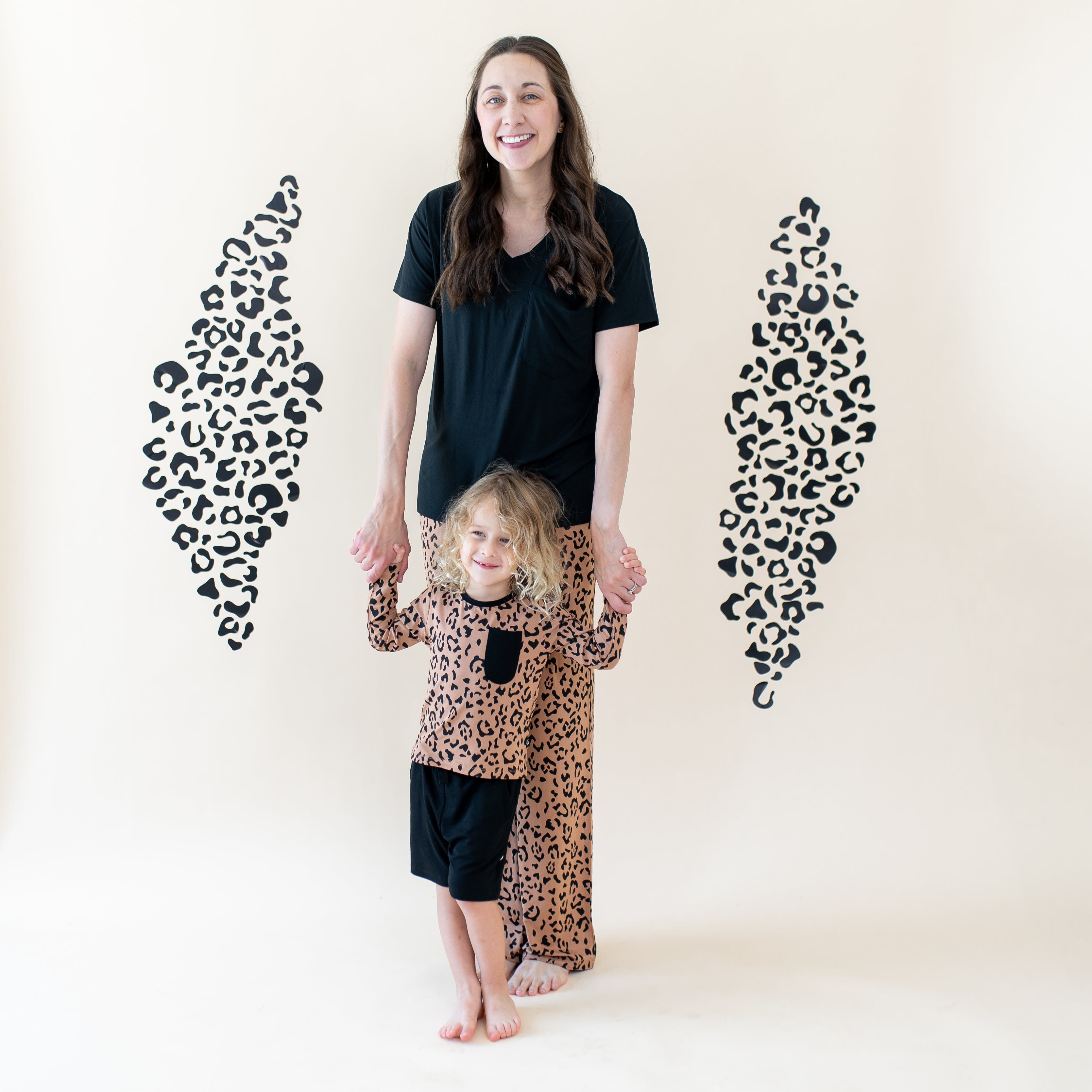Mother wearing the Women's V-neck and Latte Leopard lounge pants holding her child's hands wearing the Long Sleeve Toddler Crew Neck Tee in Latte Leopard and midnight drawstring shorts