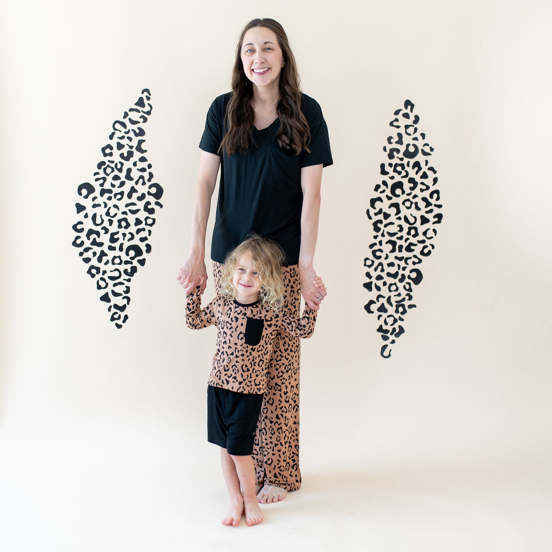 Mother wearing the Women's V-neck and Latte Leopard lounge pants holding her child's hands wearing the Long Sleeve Toddler Crew Neck Tee in Latte Leopard and midnight drawstring shorts