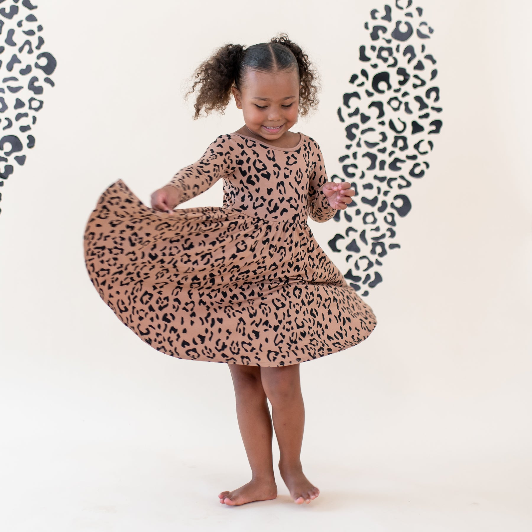 Girl twirling in her Long Sleeve Twirl Dress in Latte Leopard in front of a light colored leopard print backdrop