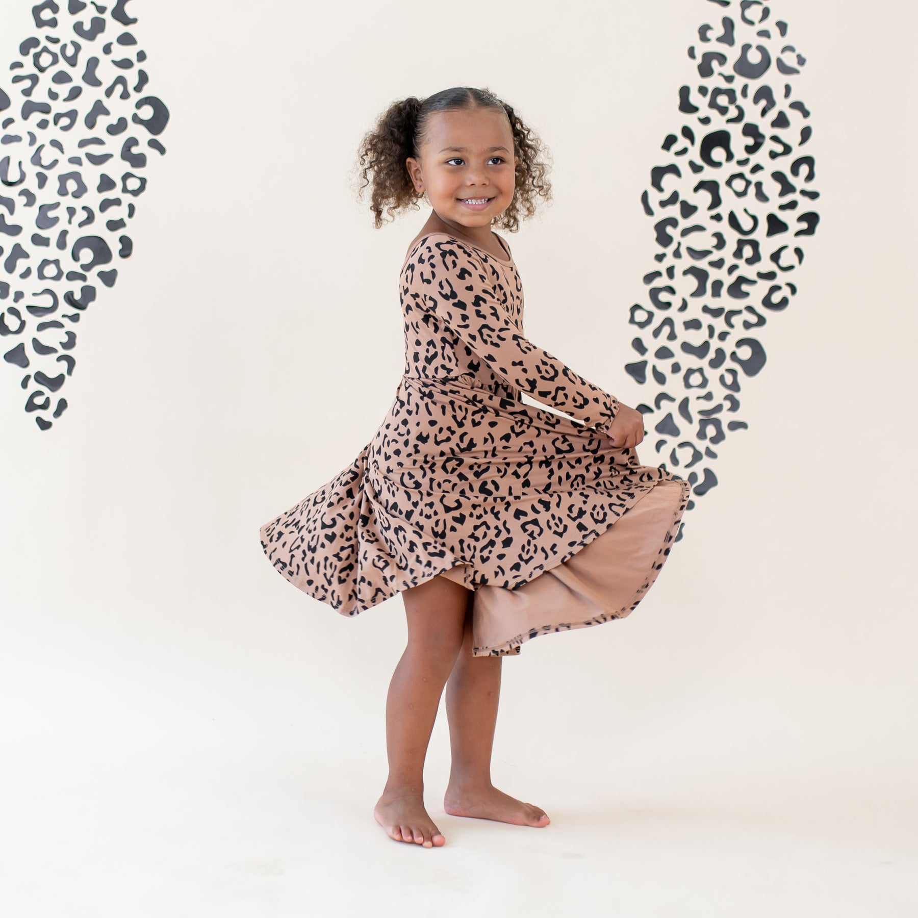 Young girl twirling in her Long Sleeve Twirl Dress in Latte Leopard in front of a light leopard print backdrop