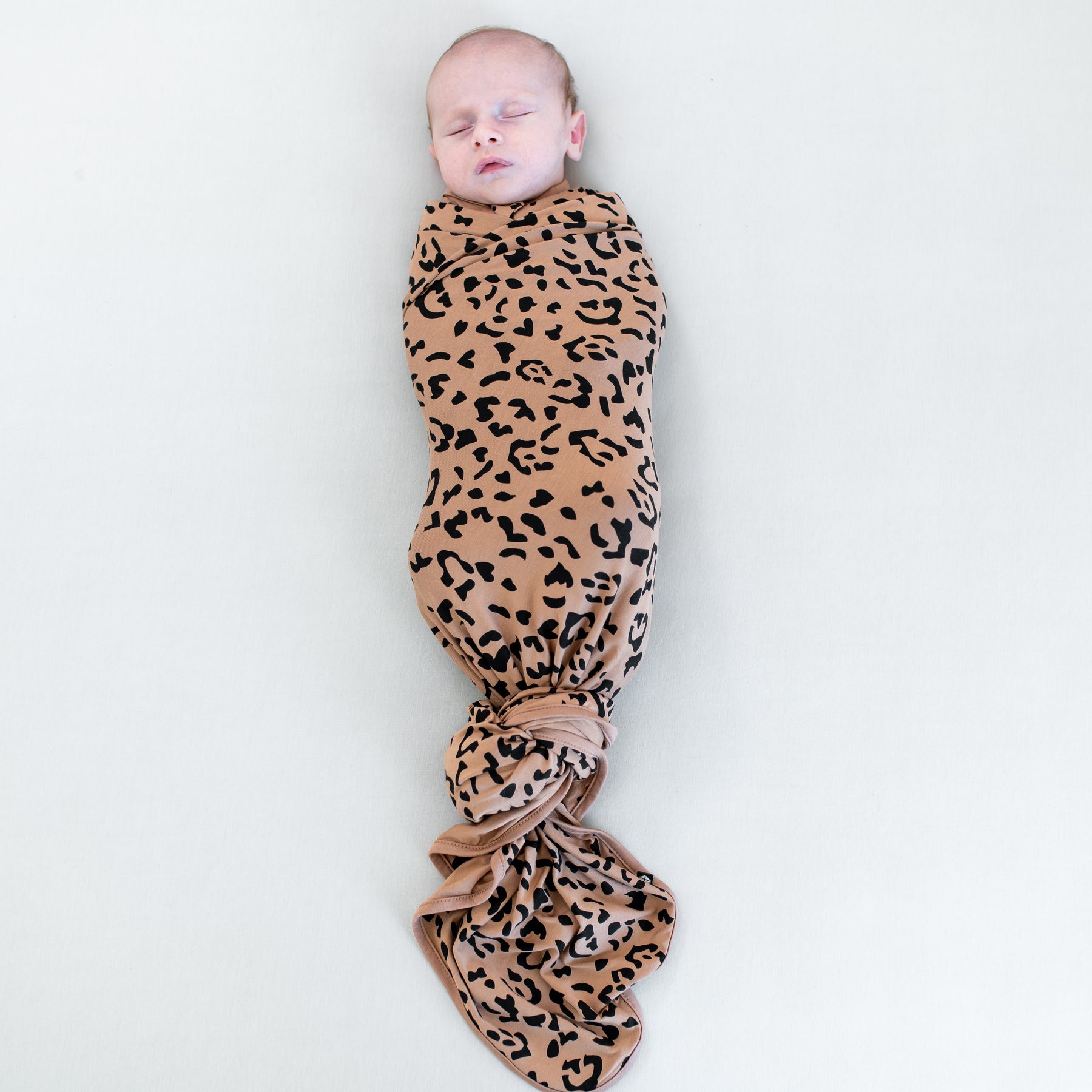 Sleeping infant swaddled in the Swaddle Blanket in Latte Leopard