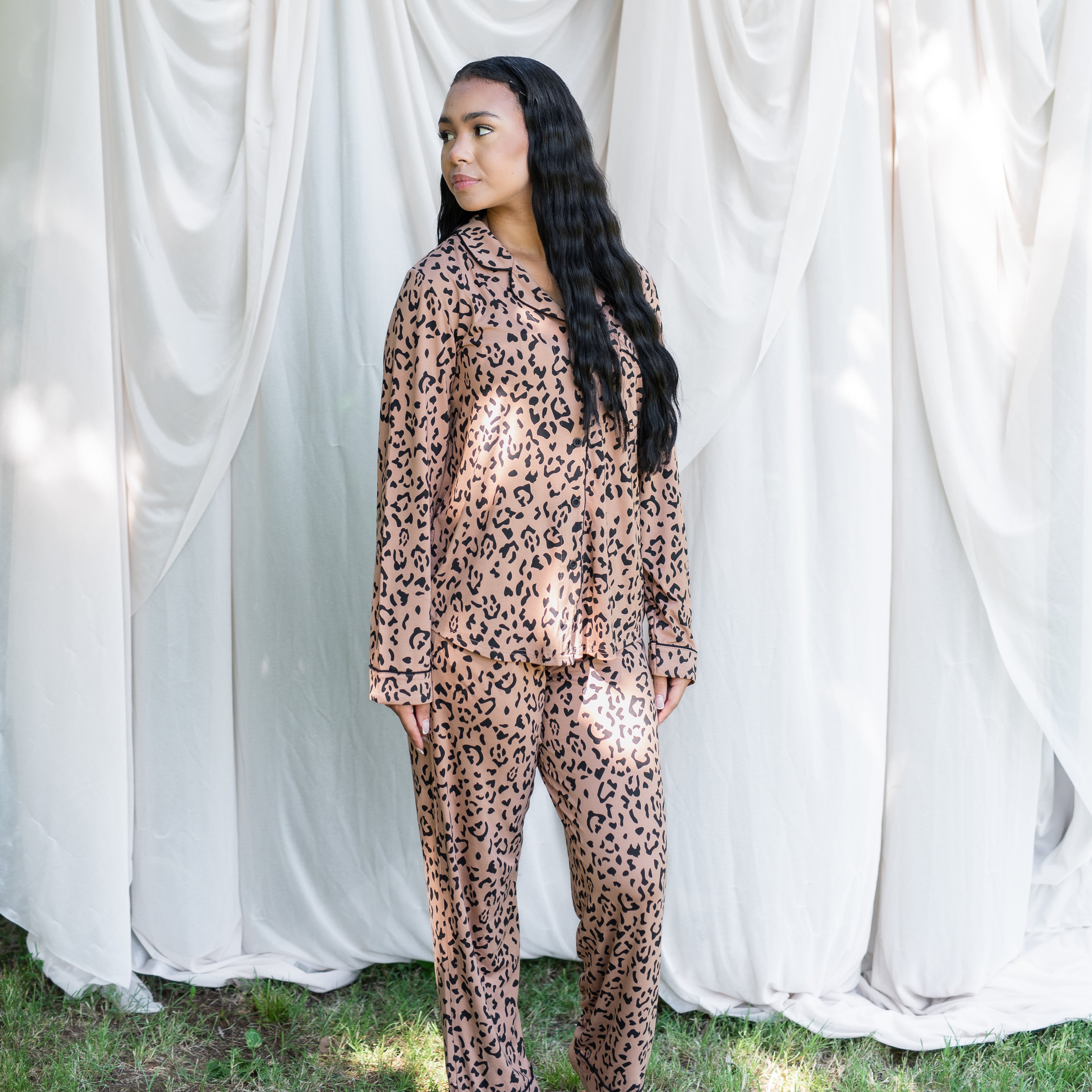 Female model looking over her shoulder standing in the grass and in front of a cream sheet backdrop wearing the Long-Sleeved Women's Pajama Set in Latte Leopard