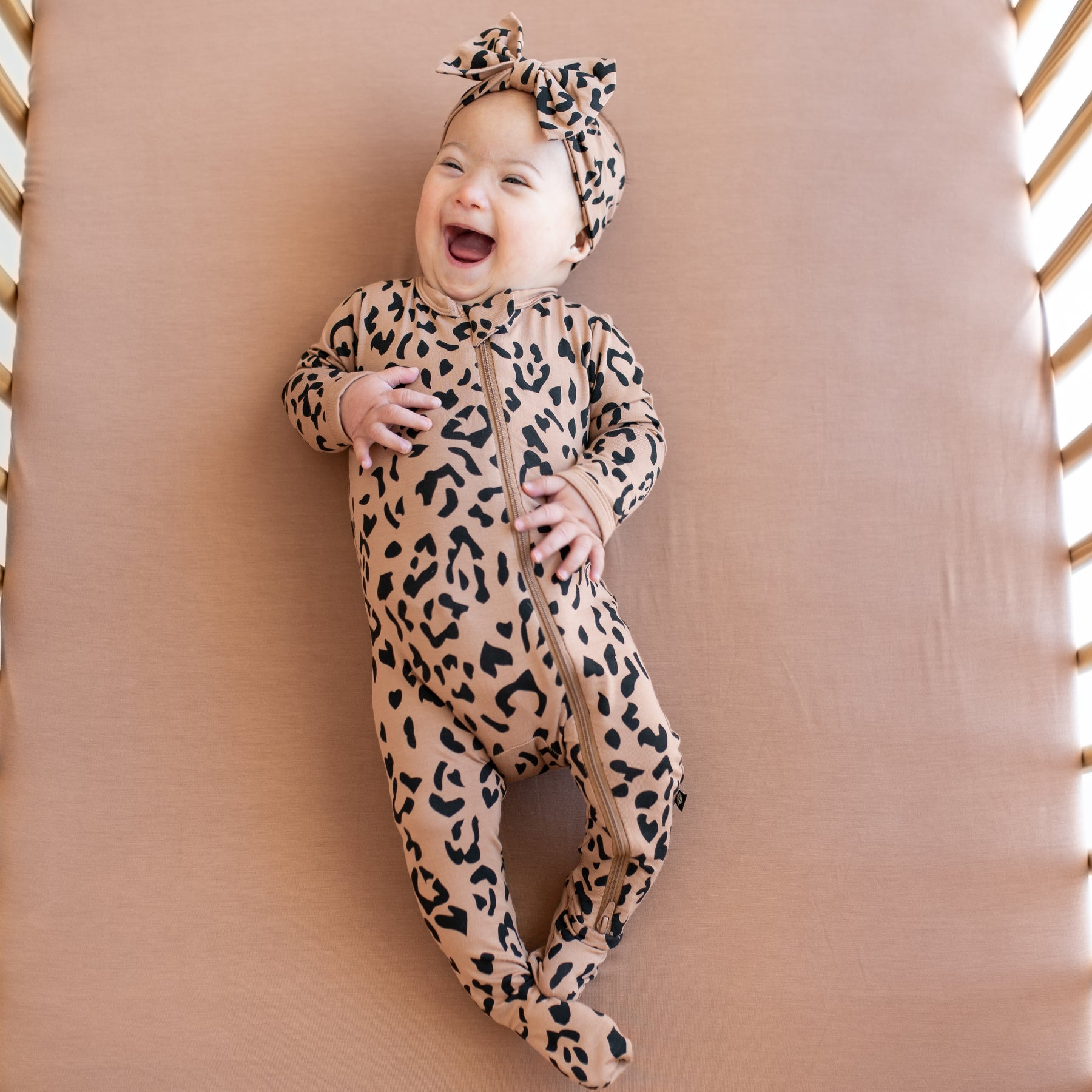 Baby wearing Zippered Footie in Latte Leopard with matching bow headband