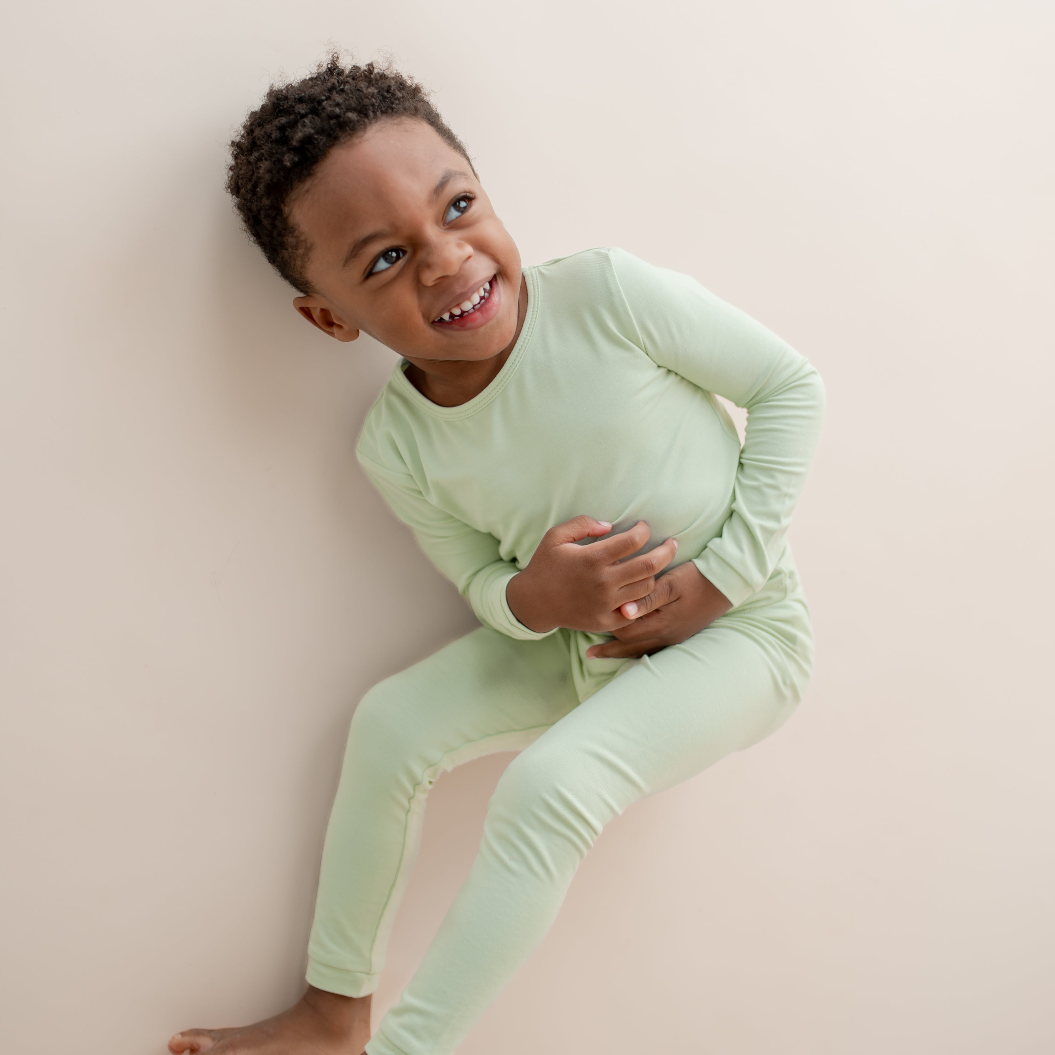 Child wearing light green pajamas laying on a neutral background
