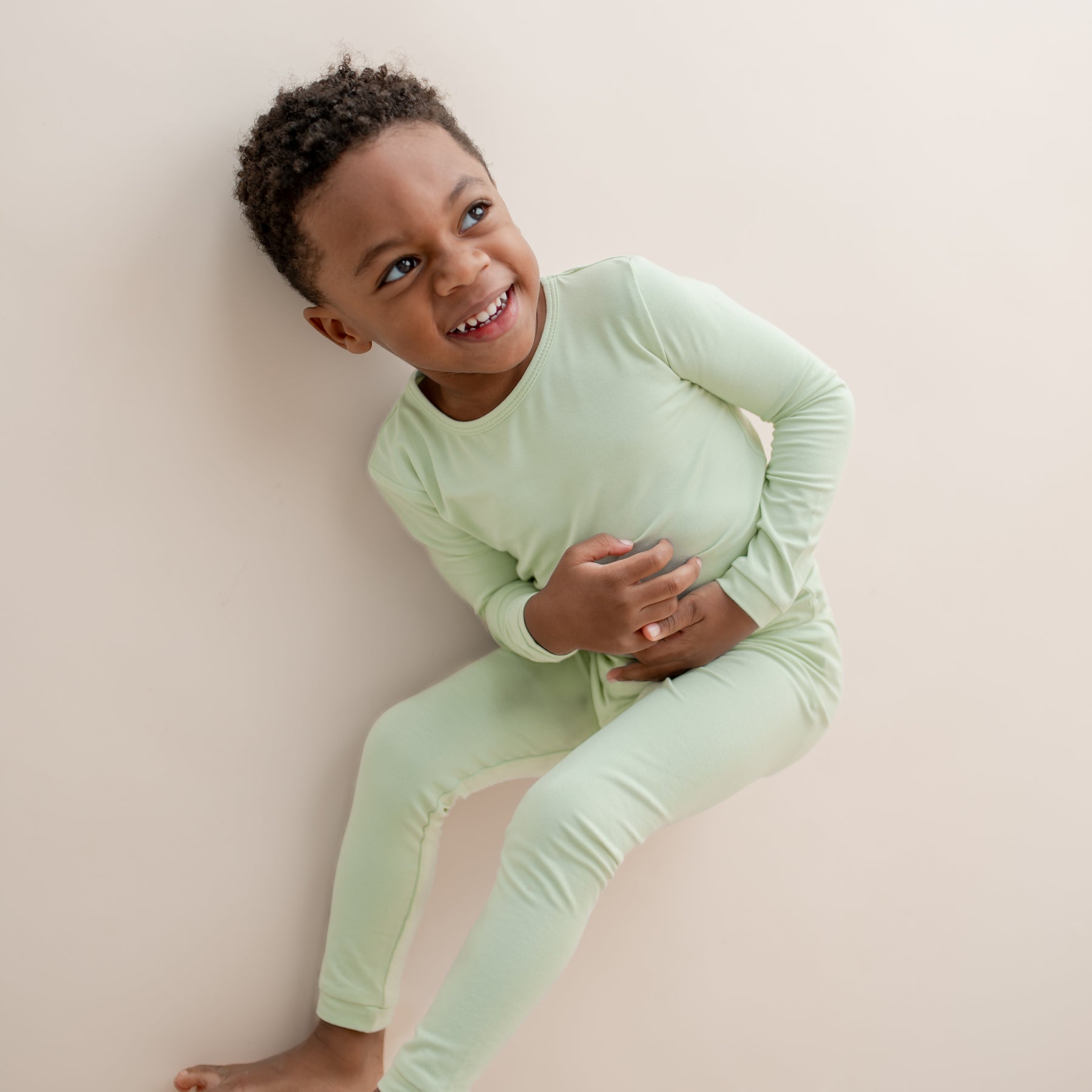 Child wearing light green pajamas laying on a neutral background