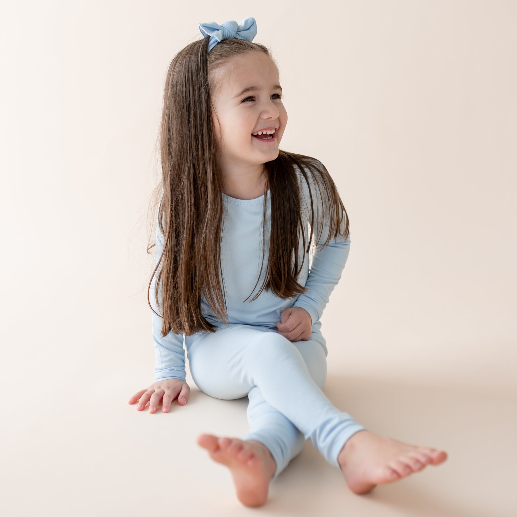 Young girl wearing a light blue outfit with a matching headband, sitting on a beige surface.