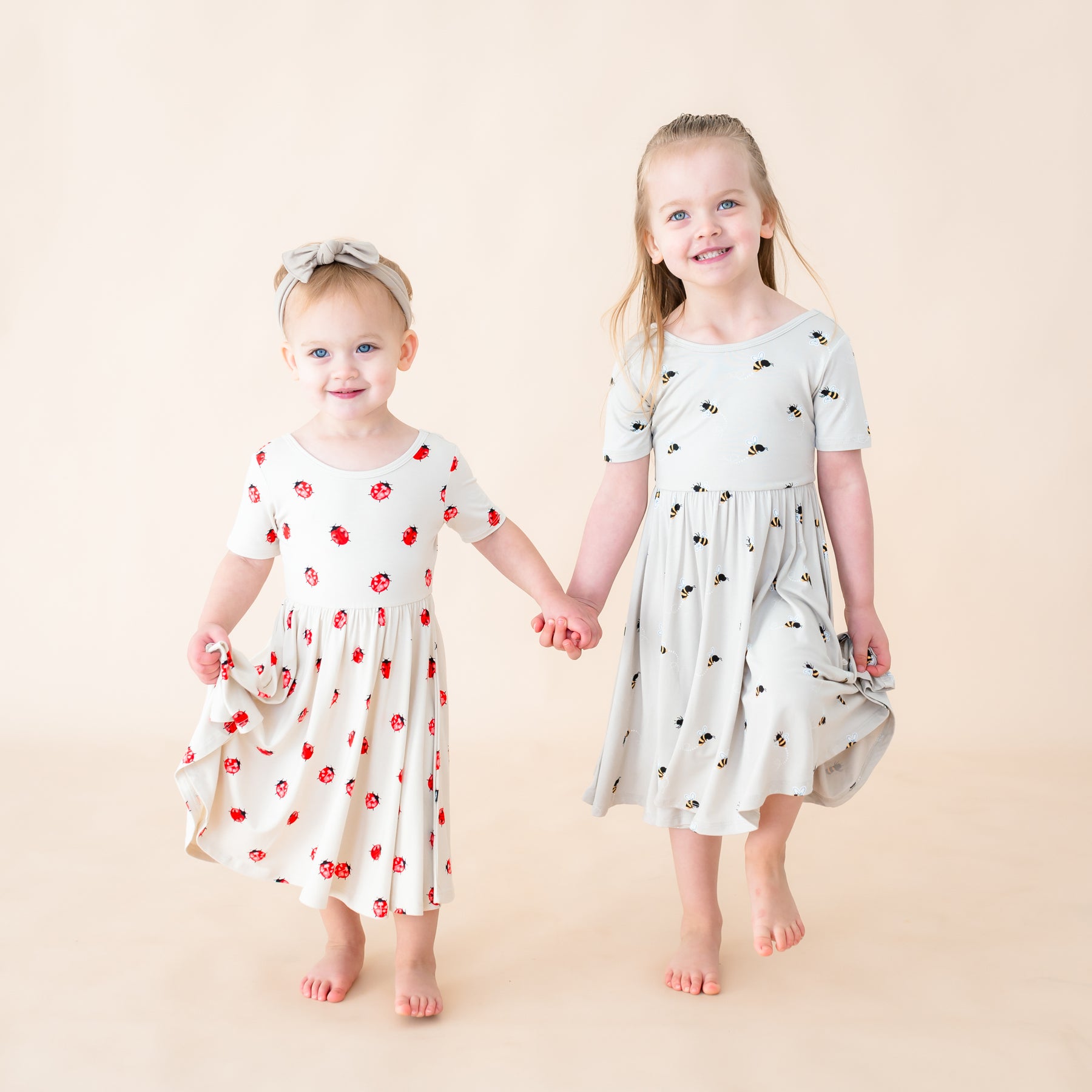 Two toddlers holding hands in twirl dresses in the prints Love Bug and Bee Mine