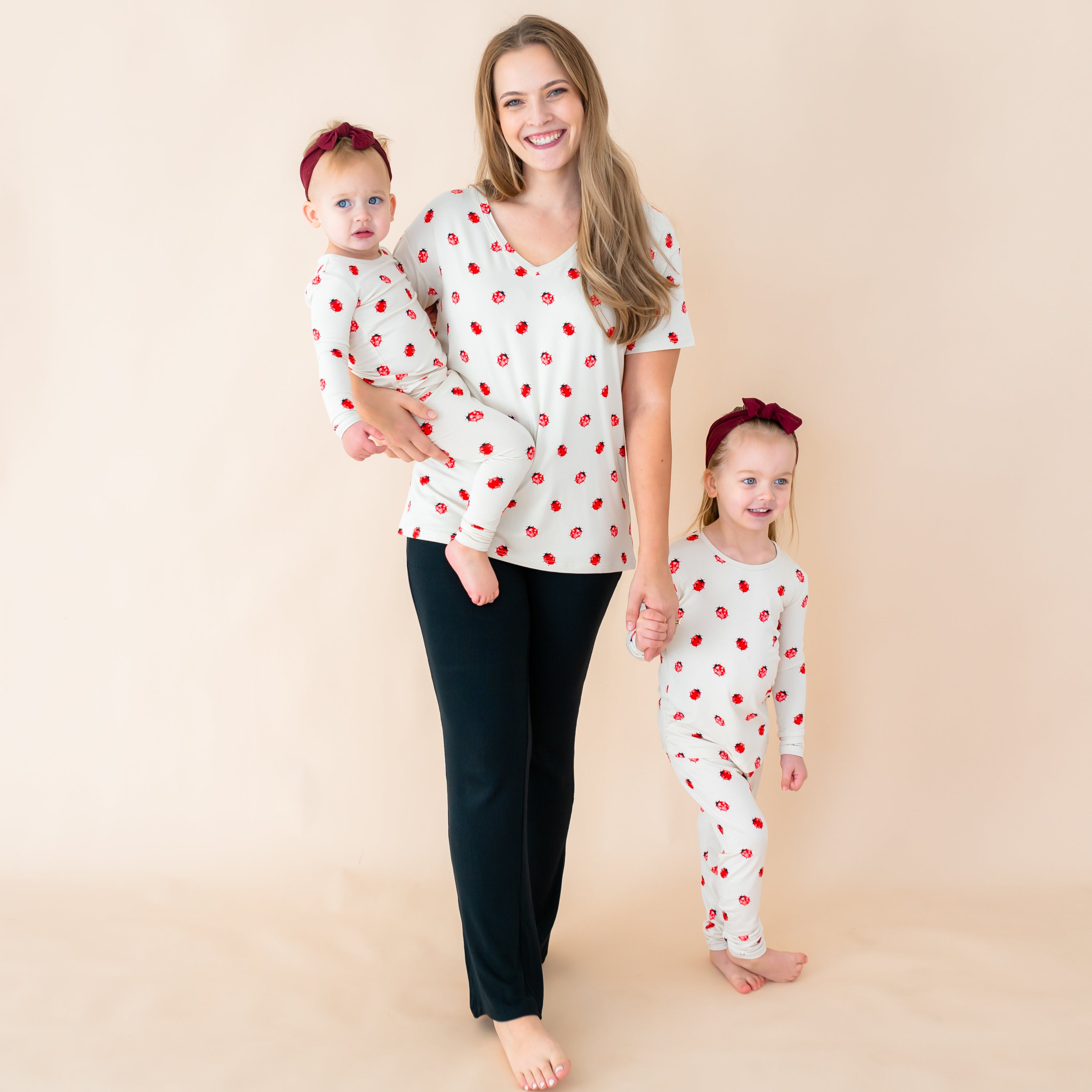 Mom wearing Love Bug v-neck holding a toddler and holding hands with another toddler both wearing Love Bug long sleeve pajamas 