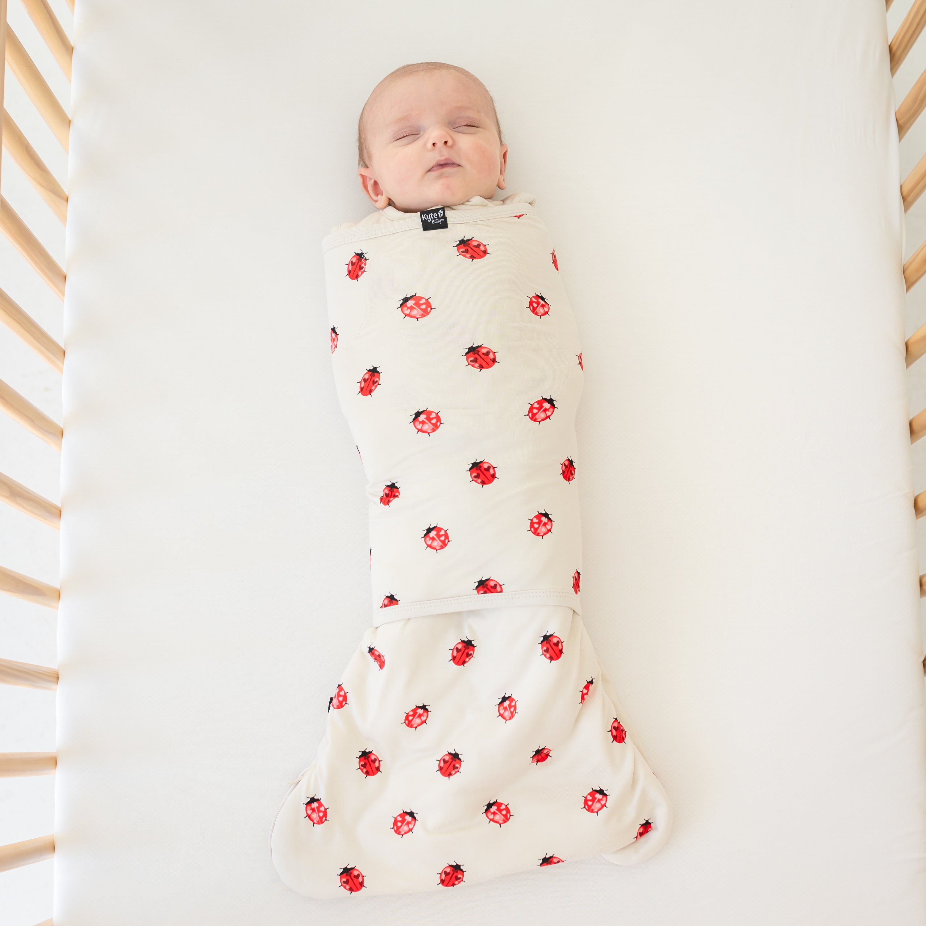 Baby wearing sleep bag swaddler in love bug laying in a crib