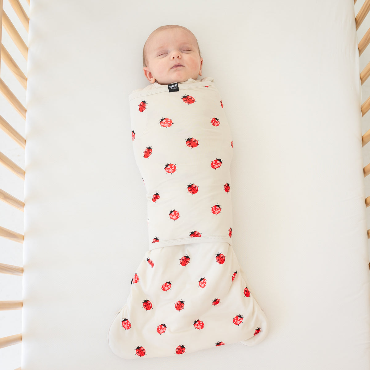 Baby wearing sleep bag swaddler in love bug laying in a crib