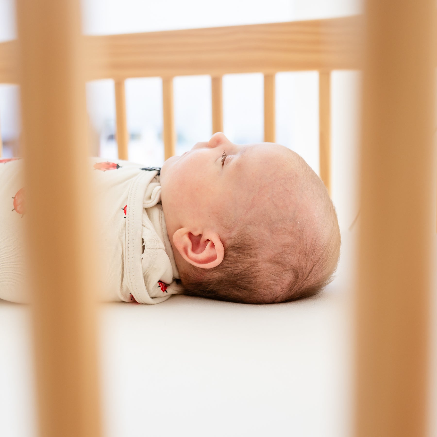 Baby sleeping wearing a sleep bag swaddler in love bug laying in a crib