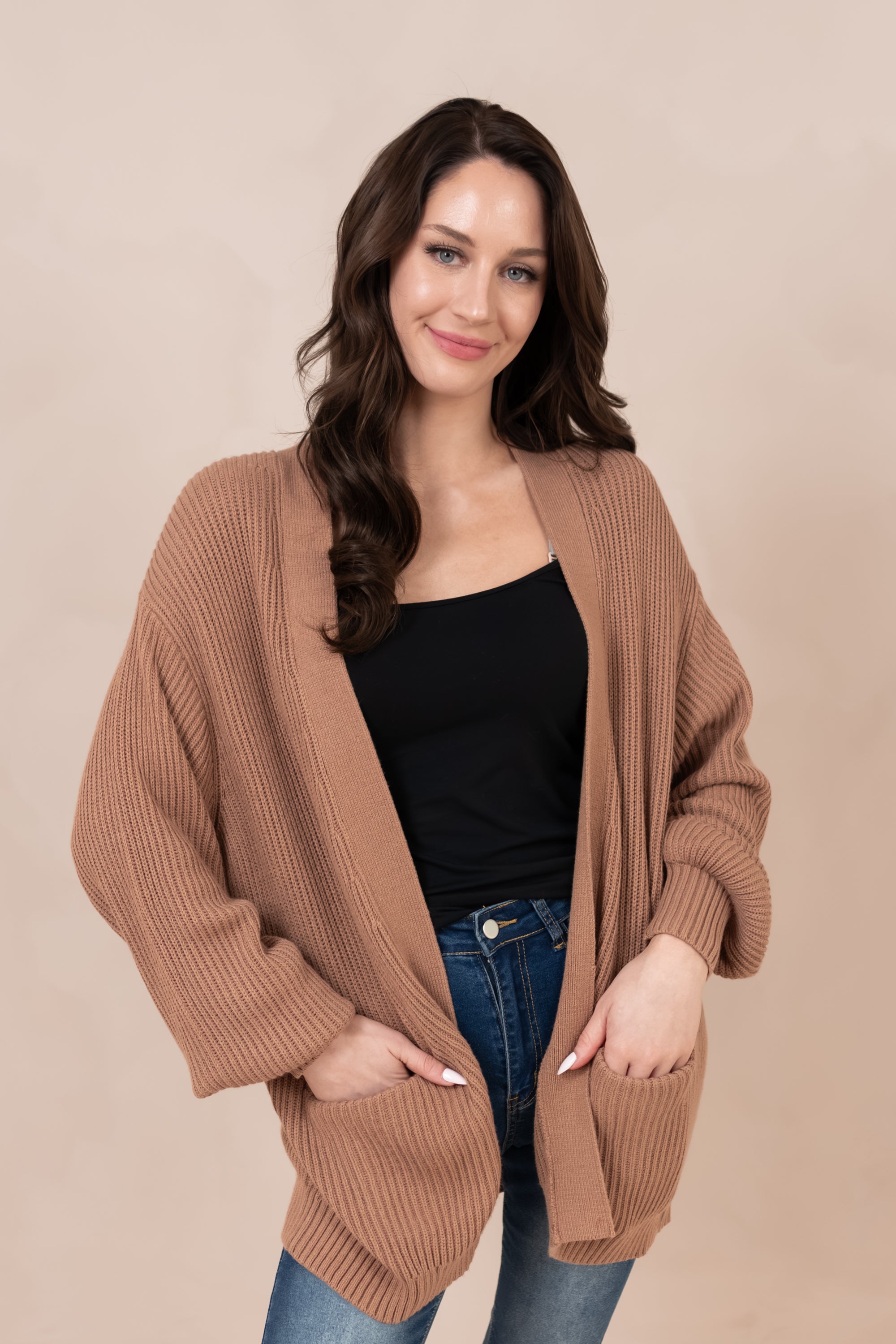 Woman wearing a brown cardigan over a black top and blue jeans on a beige background