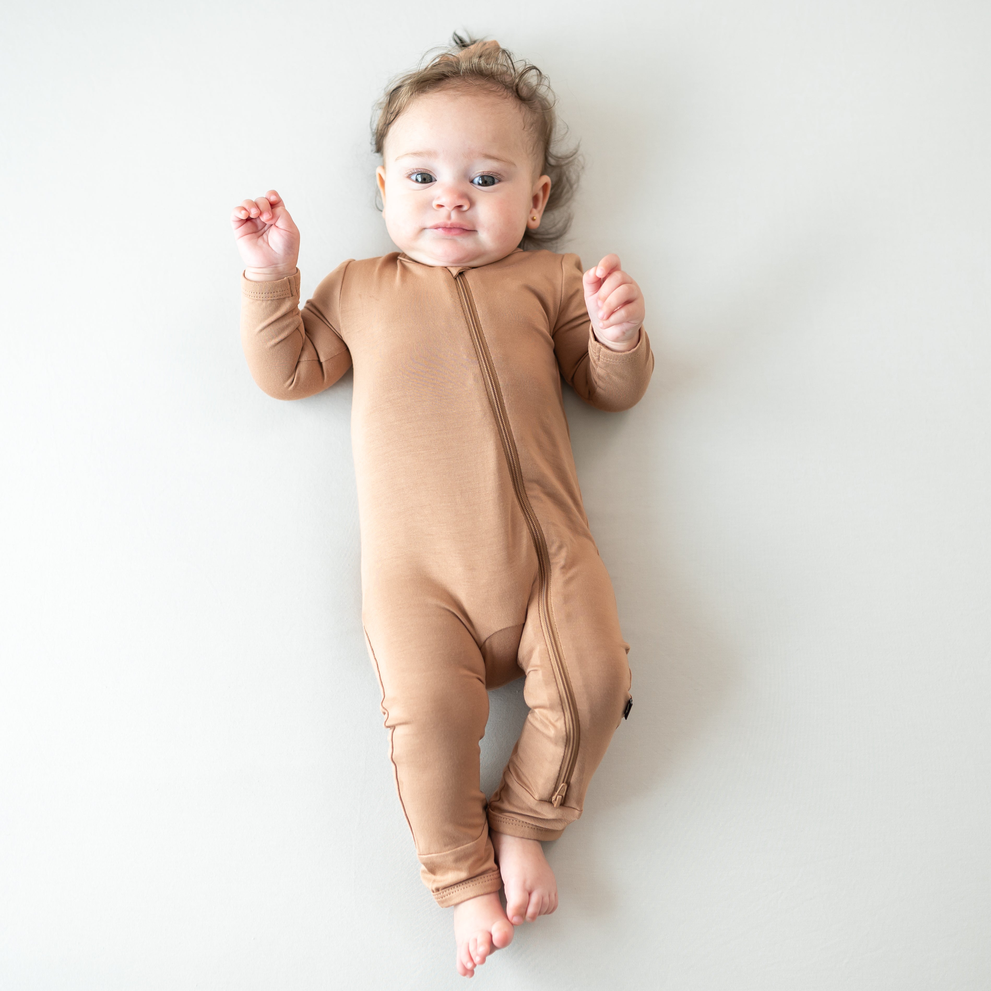 Baby wearing Zippered Romper in Latte on a neutral backdrop