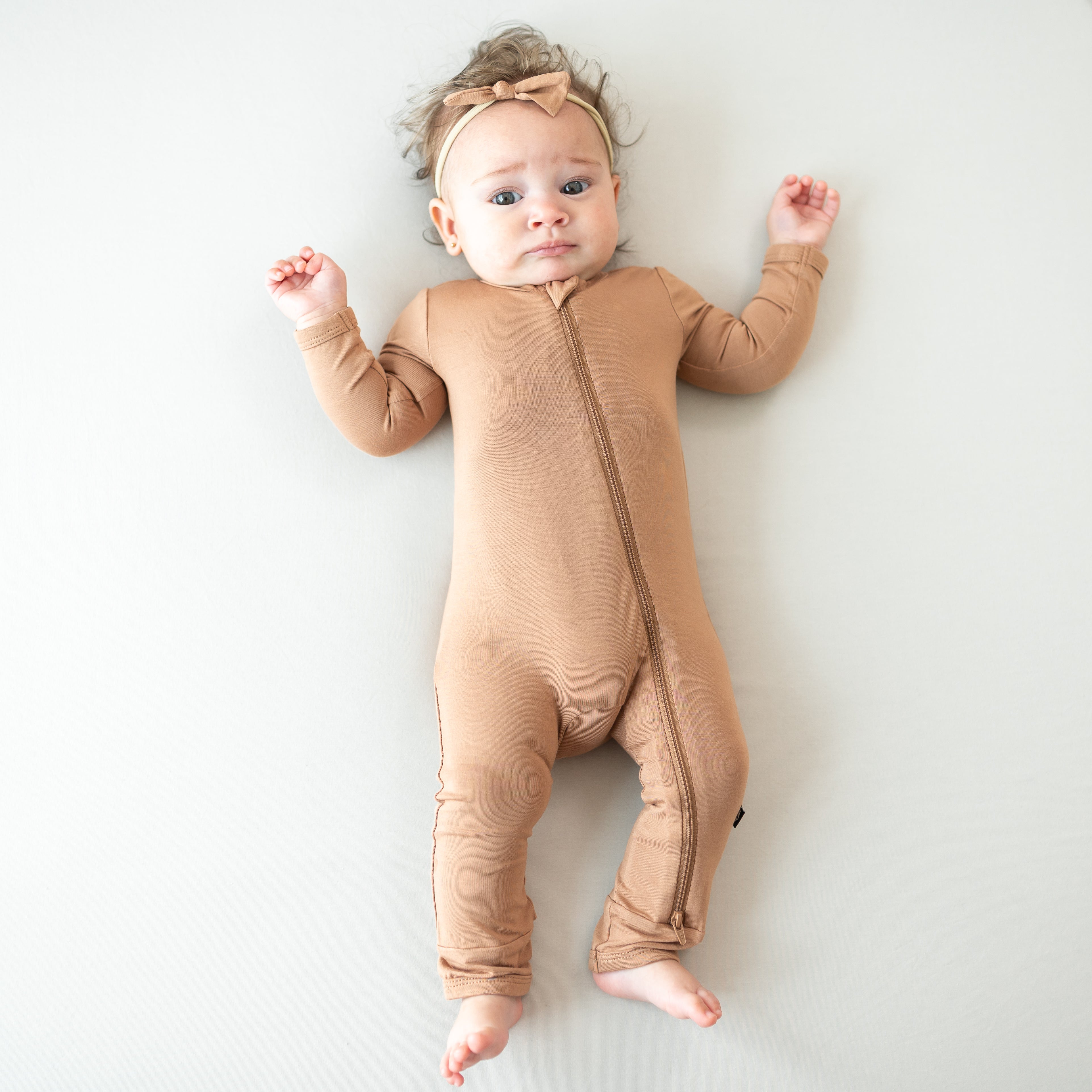 Baby wearing a bamboo zippered romper in a medium brown color on a white background
