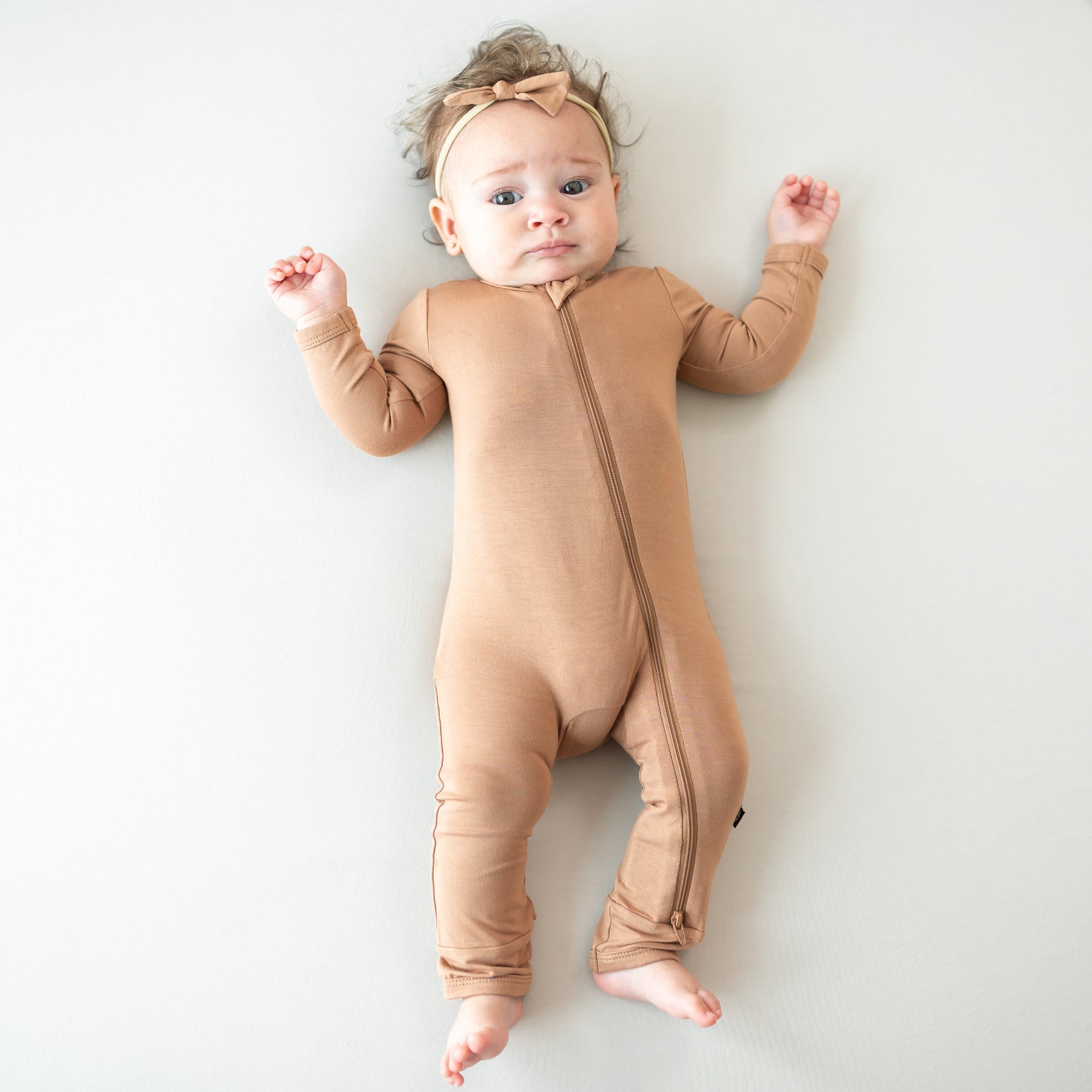Baby wearing a bamboo zippered romper in a medium brown color on a white background